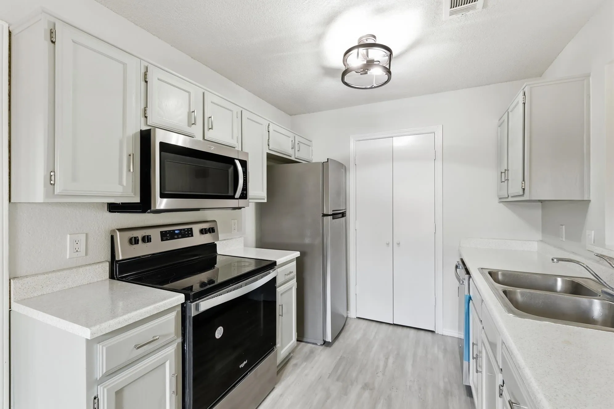 Kitchen featuring light-toned cabinetry, light countertops, wood-finish flooring, and stainless steel appliances including a range, microwave, and refrigerator