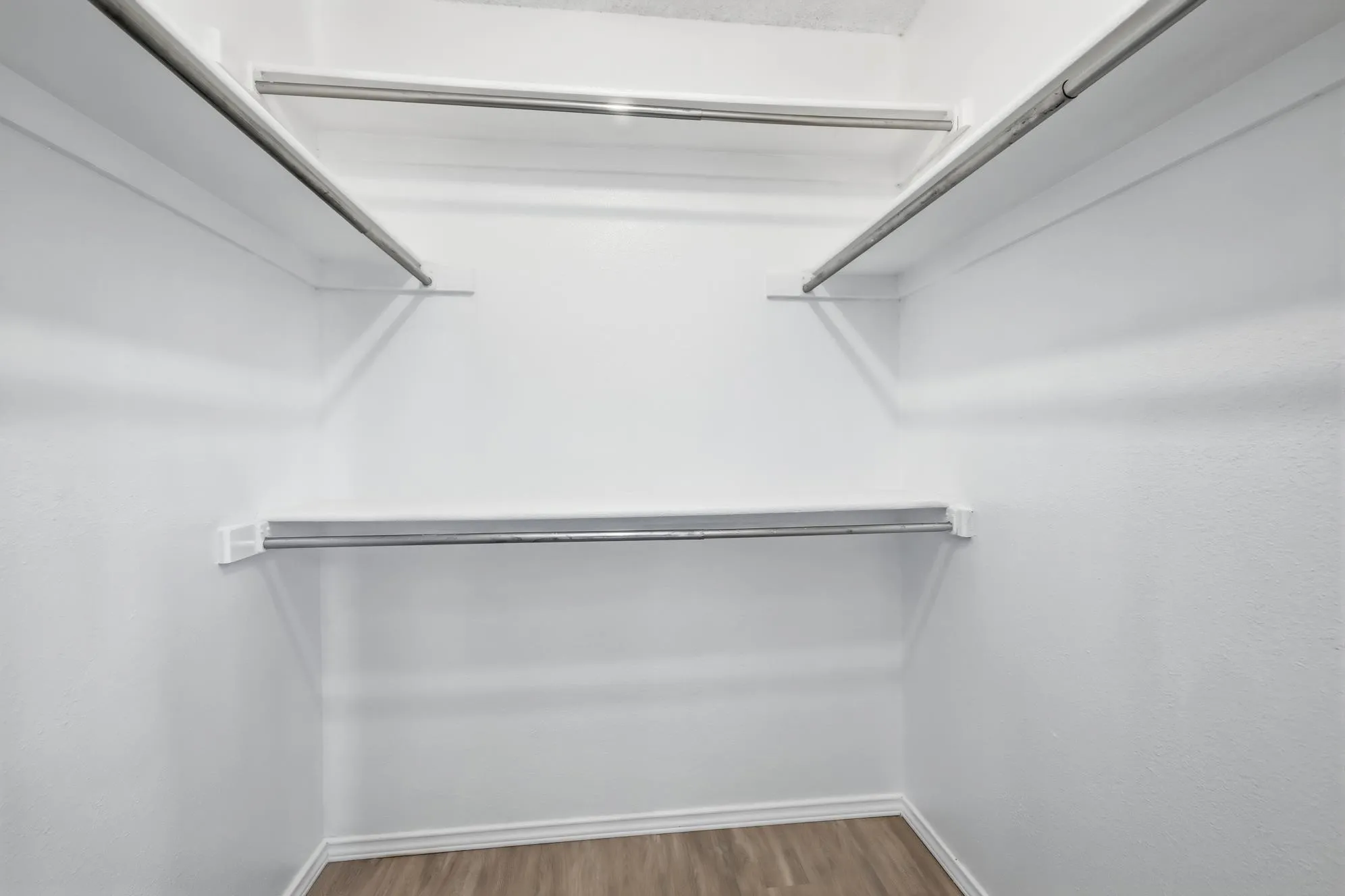 Walk-in closet featuring white painted walls, wood-finish flooring, and multiple levels of shelving and clothing rods for ample storage