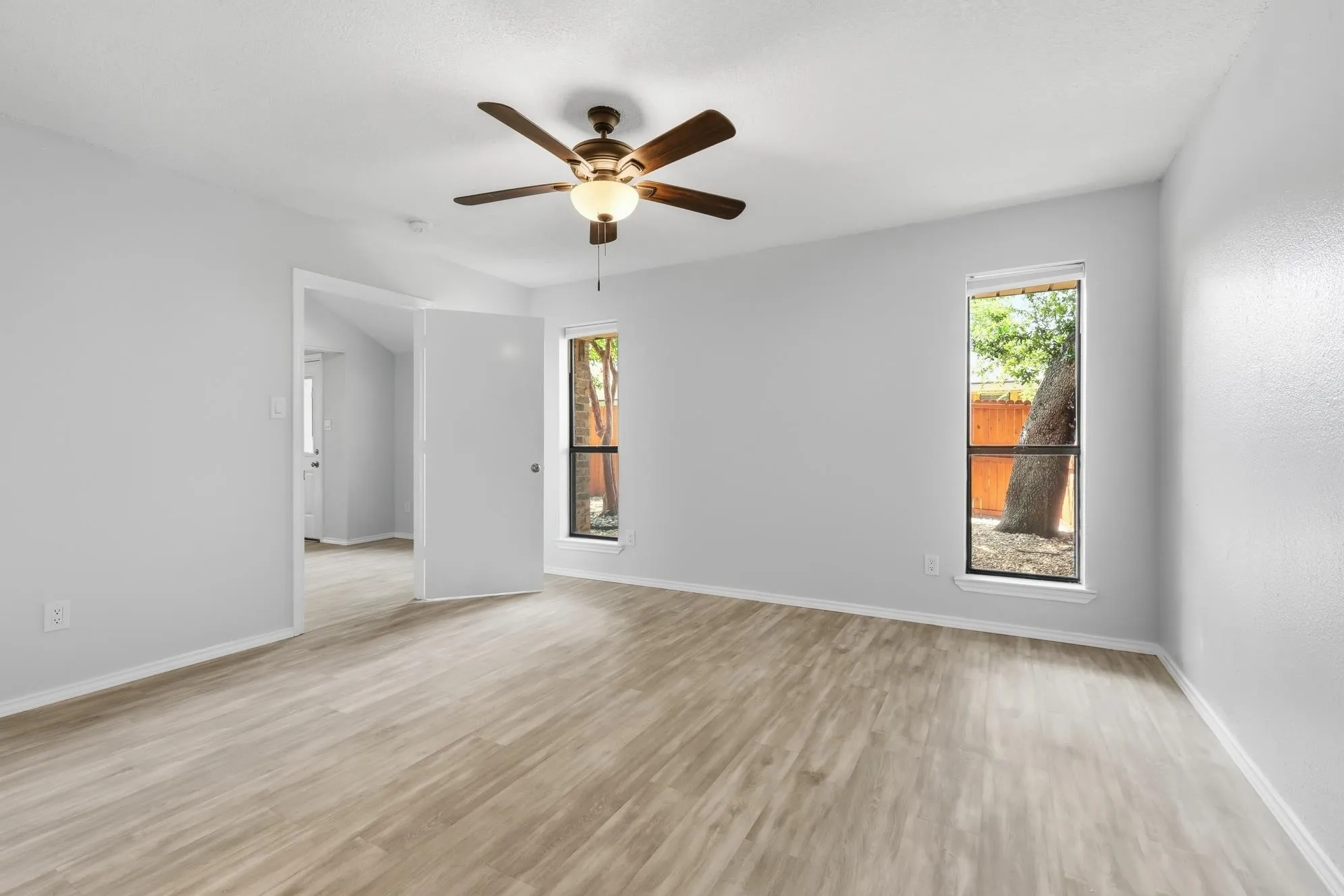 Spacious room featuring light wood-finish flooring, light gray wall paint, and a ceiling fan with integrated lighting