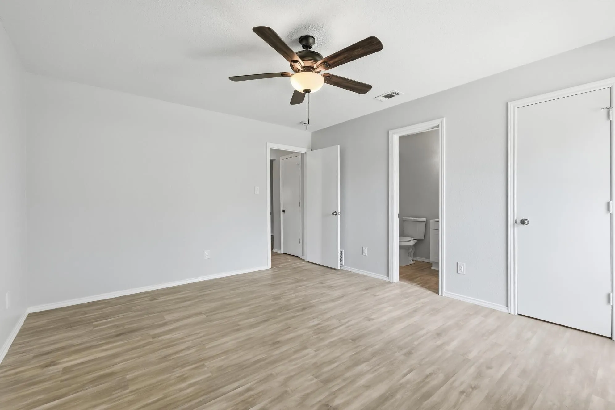 Spacious room featuring wood-finish flooring, light grey walls, and a ceiling fan with integrated lighting