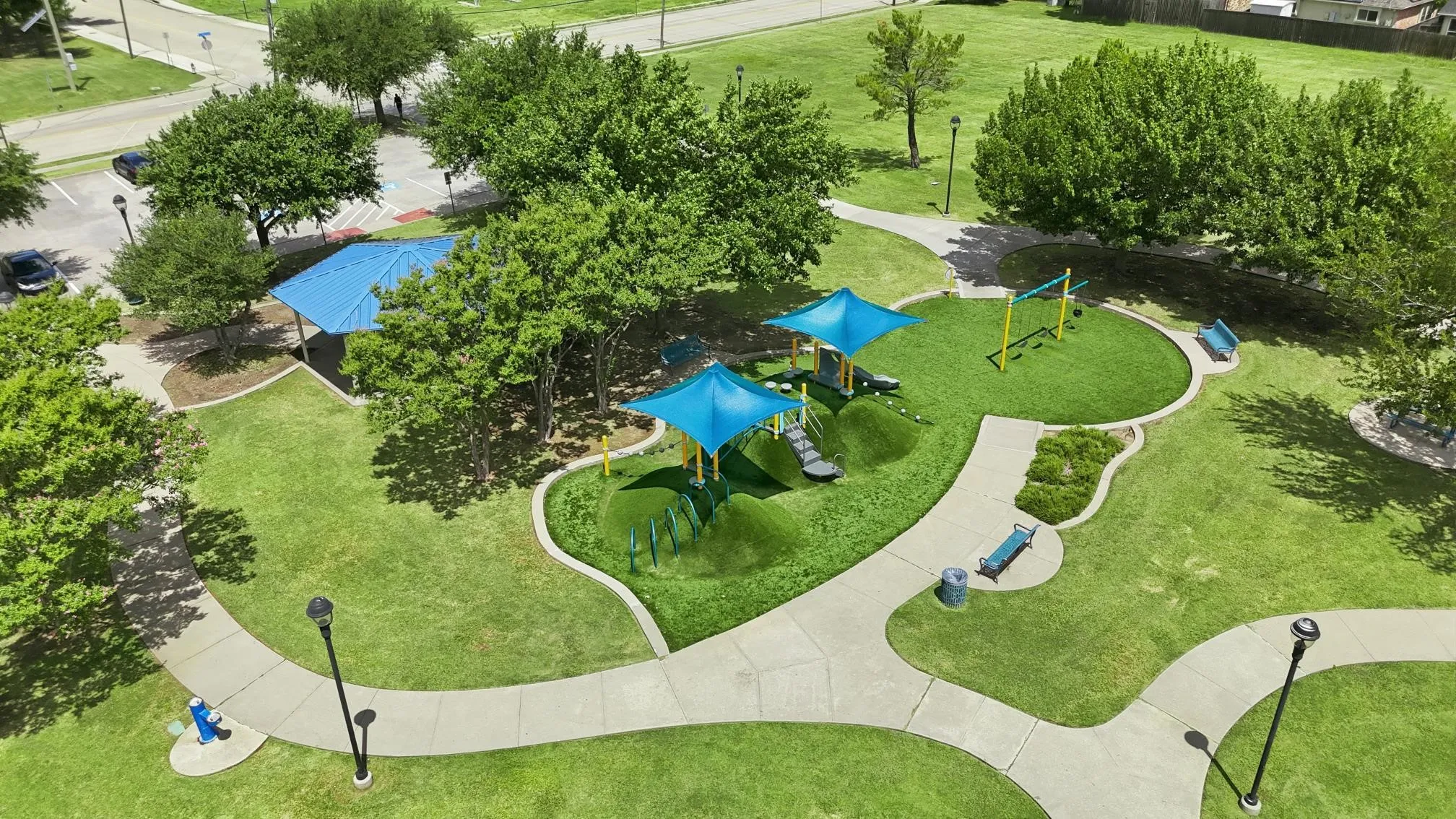 Community park featuring recreational play structures with blue canopies, concrete pathways, and mature trees. So many amenetities.