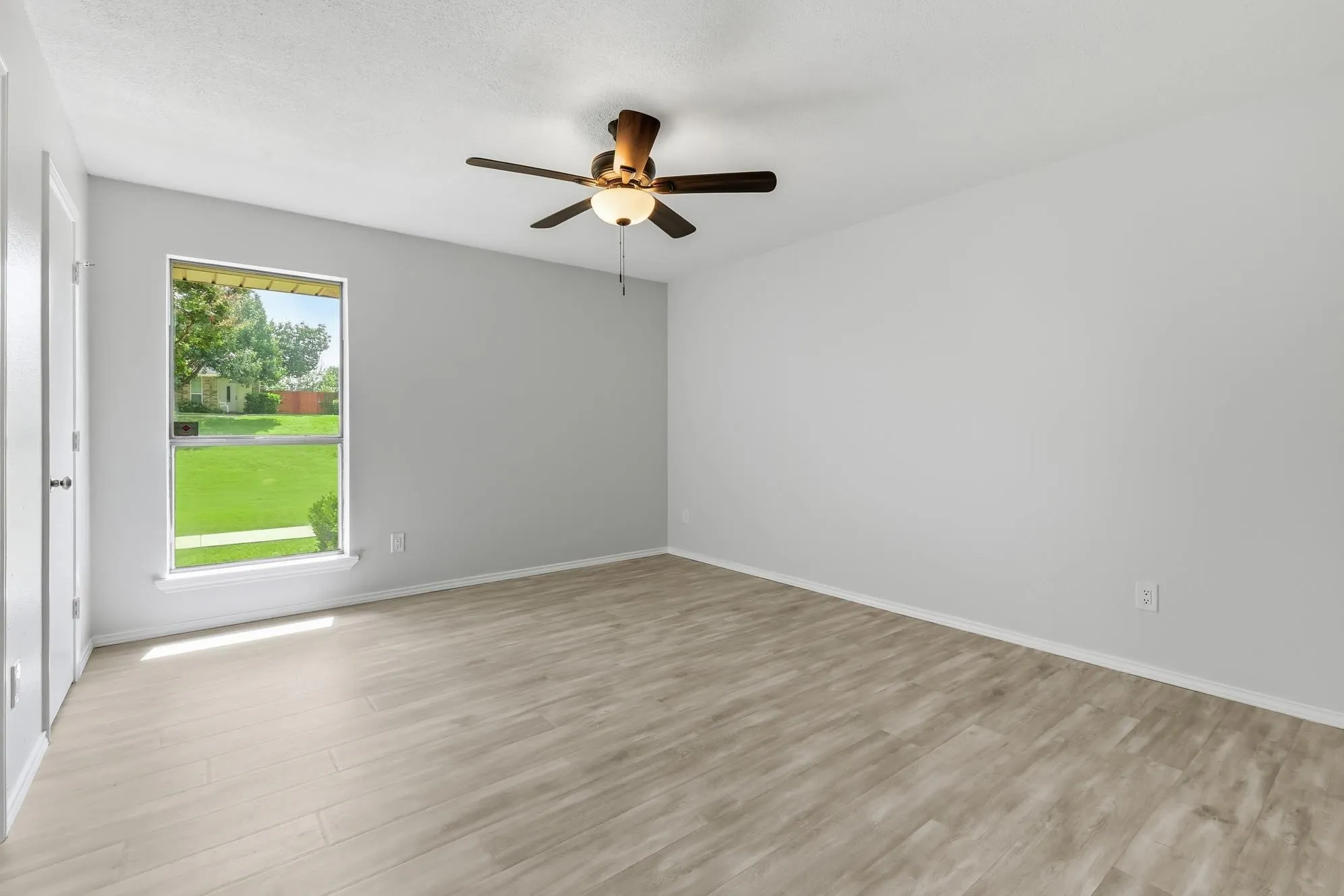 Bright and inviting secondary bedroom featuring luxury vinyl plank flooring, fresh neutral paint, a ceiling fan, and abundant natural light—creating a comfortable and versatile space for family, guests, or a home office.