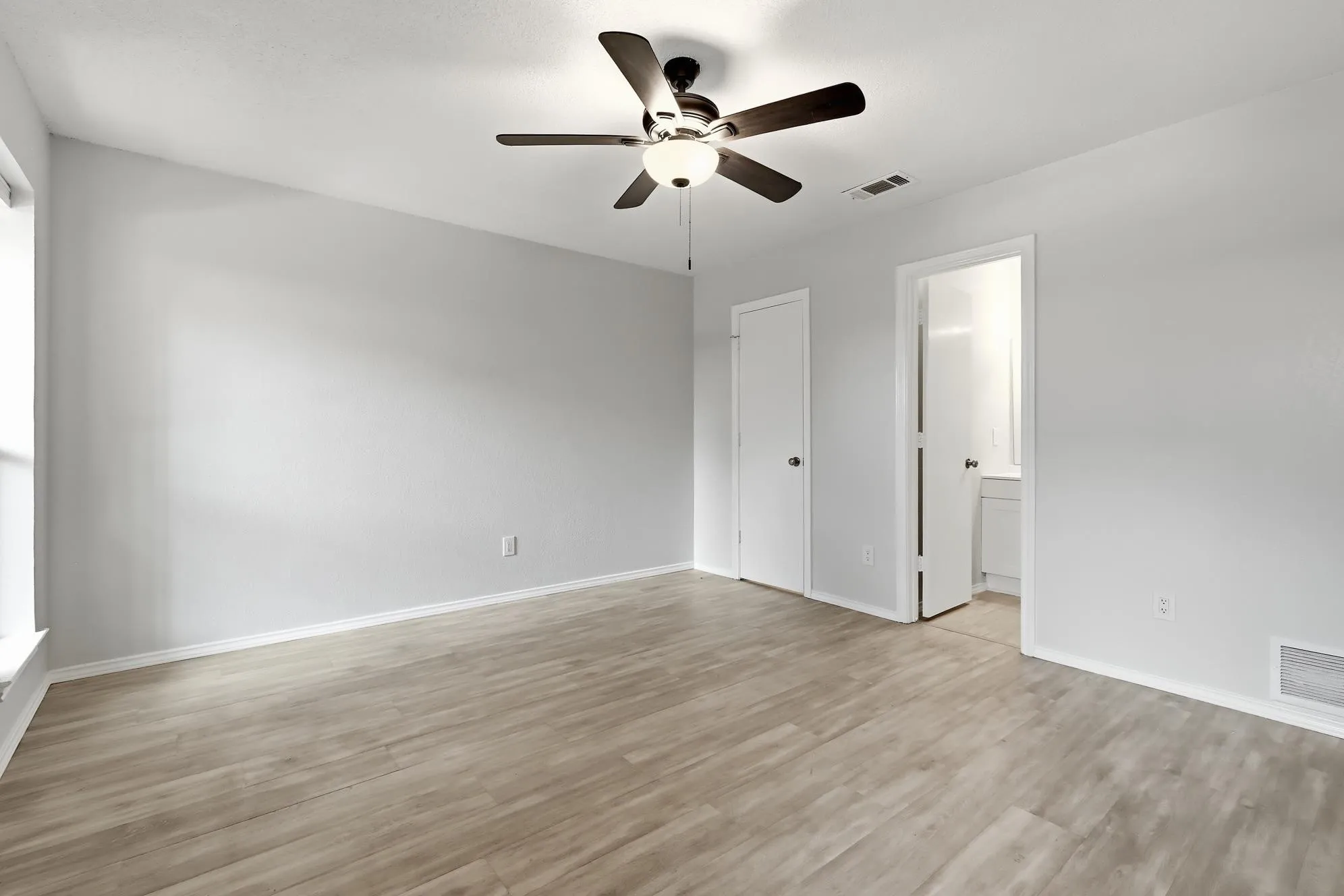Spacious room featuring wood-finish flooring, a contemporary ceiling fan with integrated lighting, and light gray wall paint