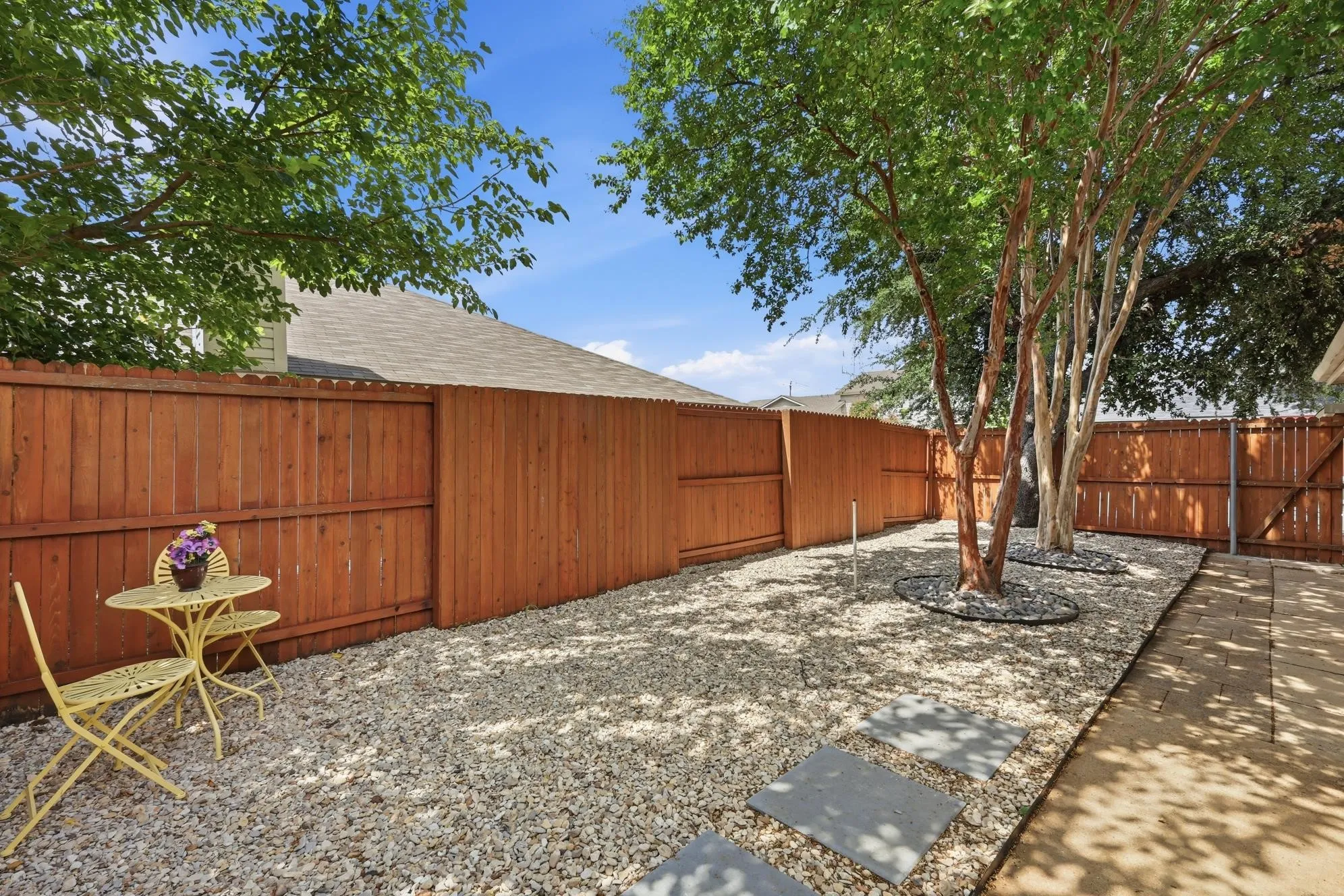 Enclosed outdoor space featuring a wood privacy fence, gravel landscaping, and mature trees