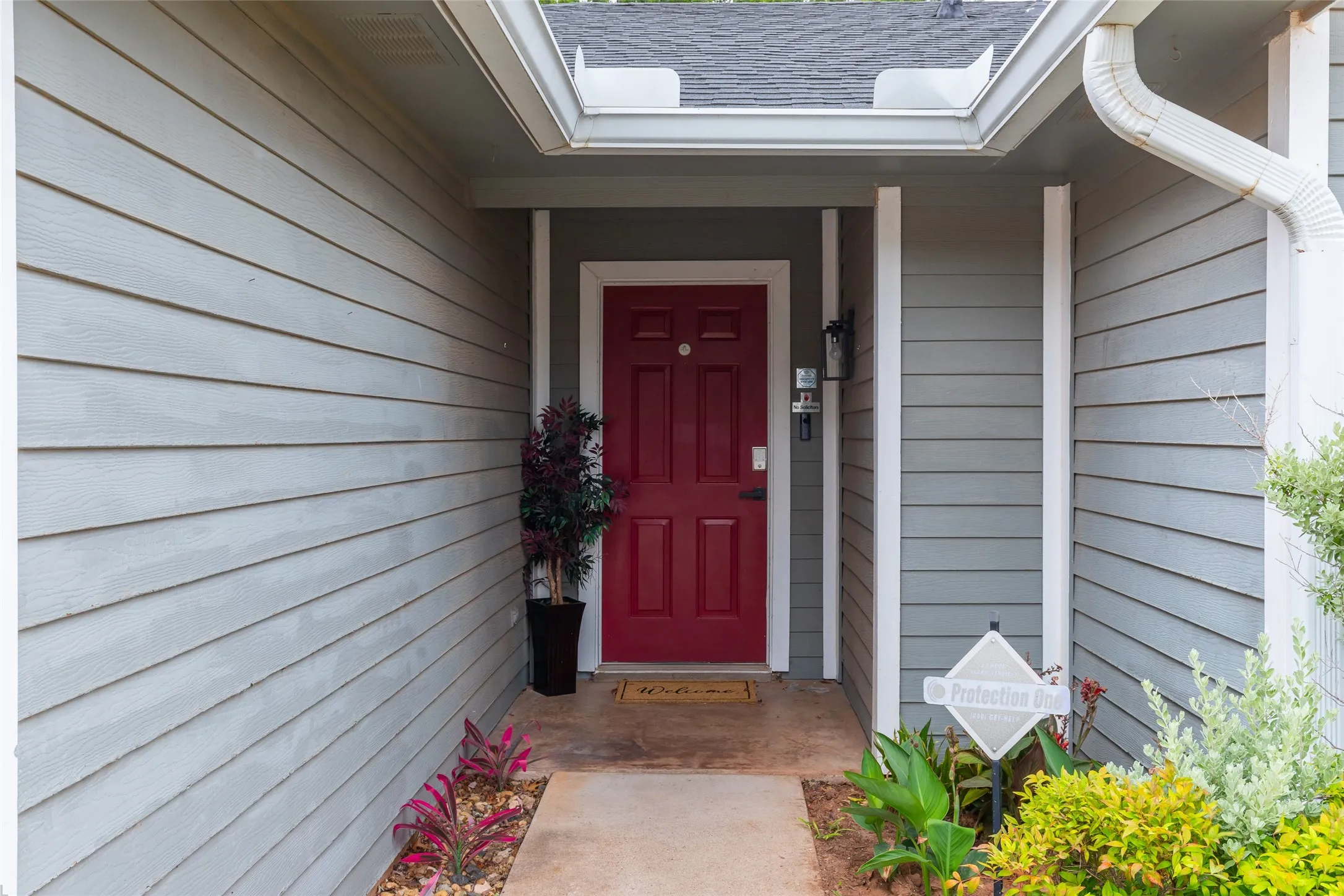 Inviting front entrance featuring a vibrant red paneled door, durable siding, an asphalt shingle roof, and a concrete walkway