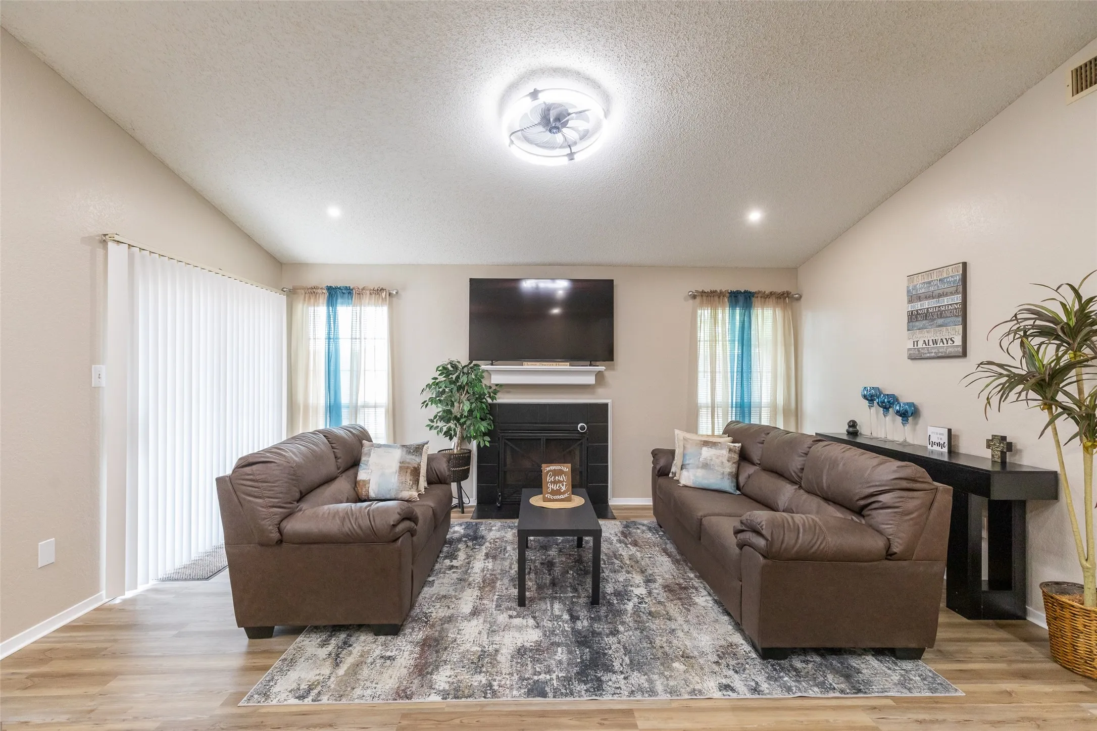 Living area featuring vaulted ceilings, wood-finish flooring, a fireplace with a white mantel, and a sliding glass door