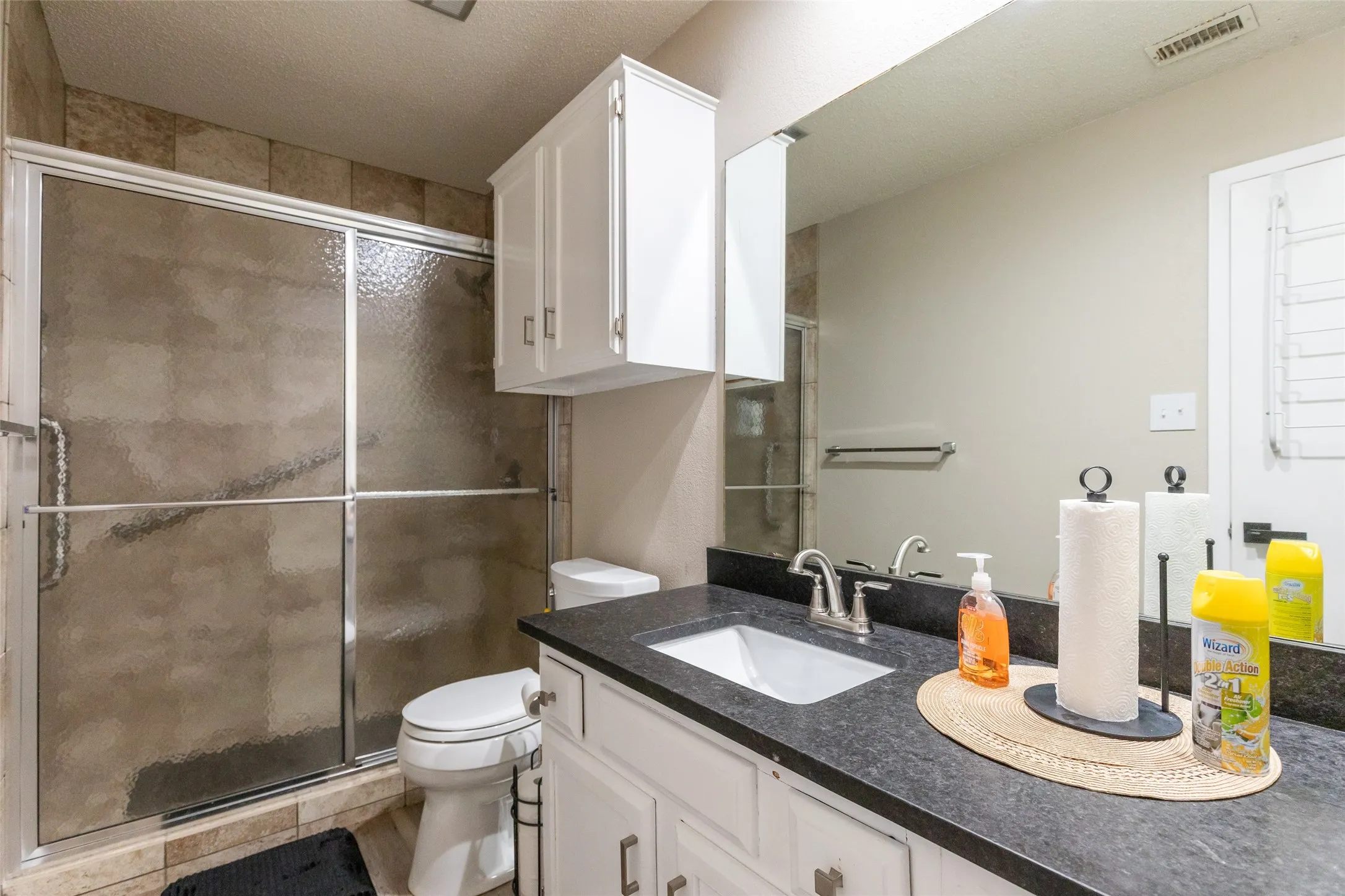 Master Bathroom featuring a glass-enclosed shower with tile surround, a vanity with a dark countertop and integrated sink, white cabinetry with silver hardware, and a large wall-mounted mirror