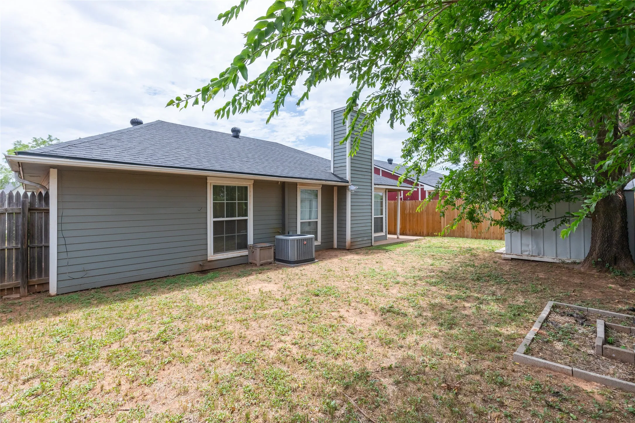 Spacious backyard featuring a large mature tree, a wooden fence, and a storage shed