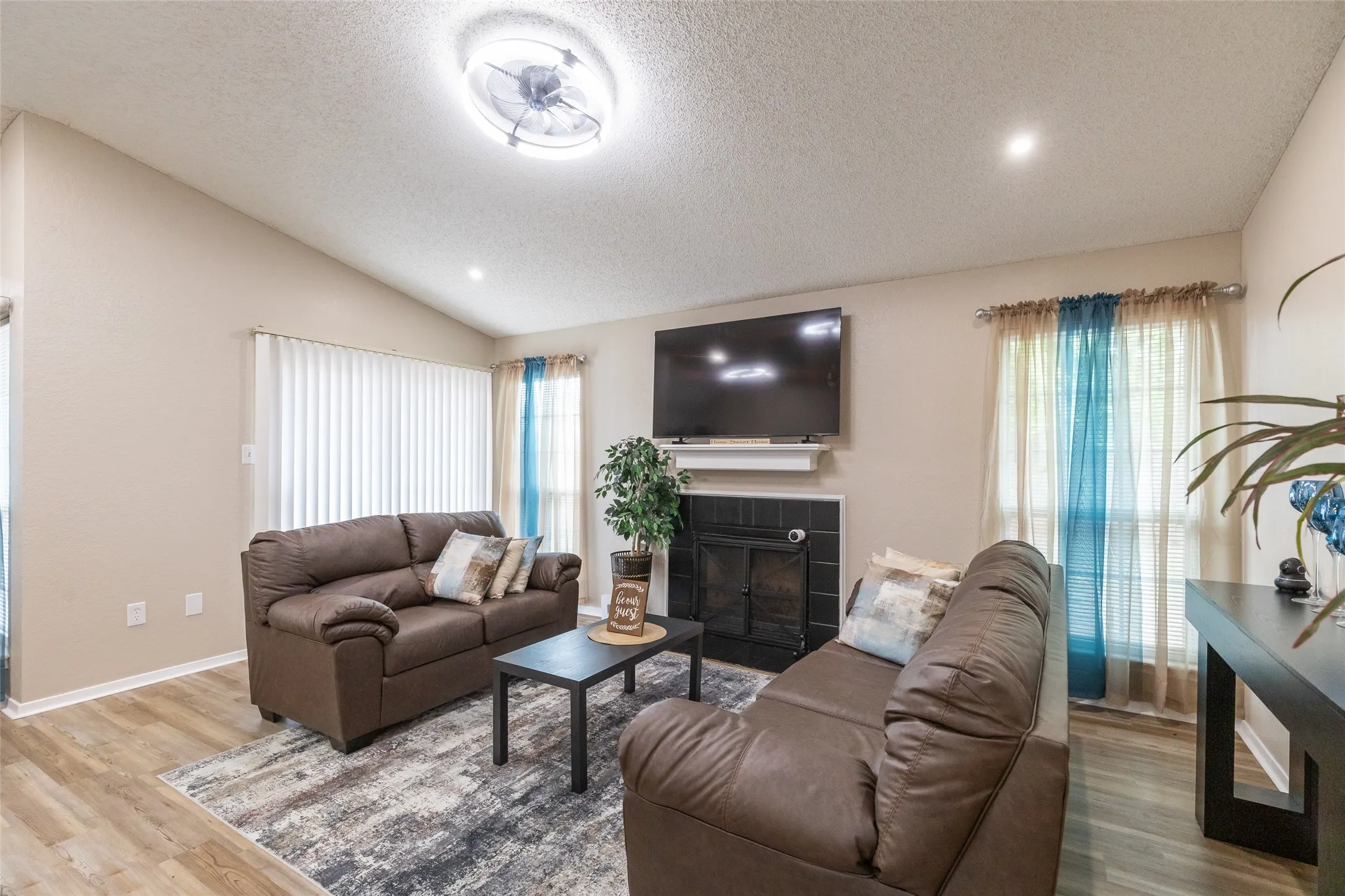 Living area featuring vaulted ceilings, wood-finish flooring, recessed lighting, and a fireplace with a black tile surround