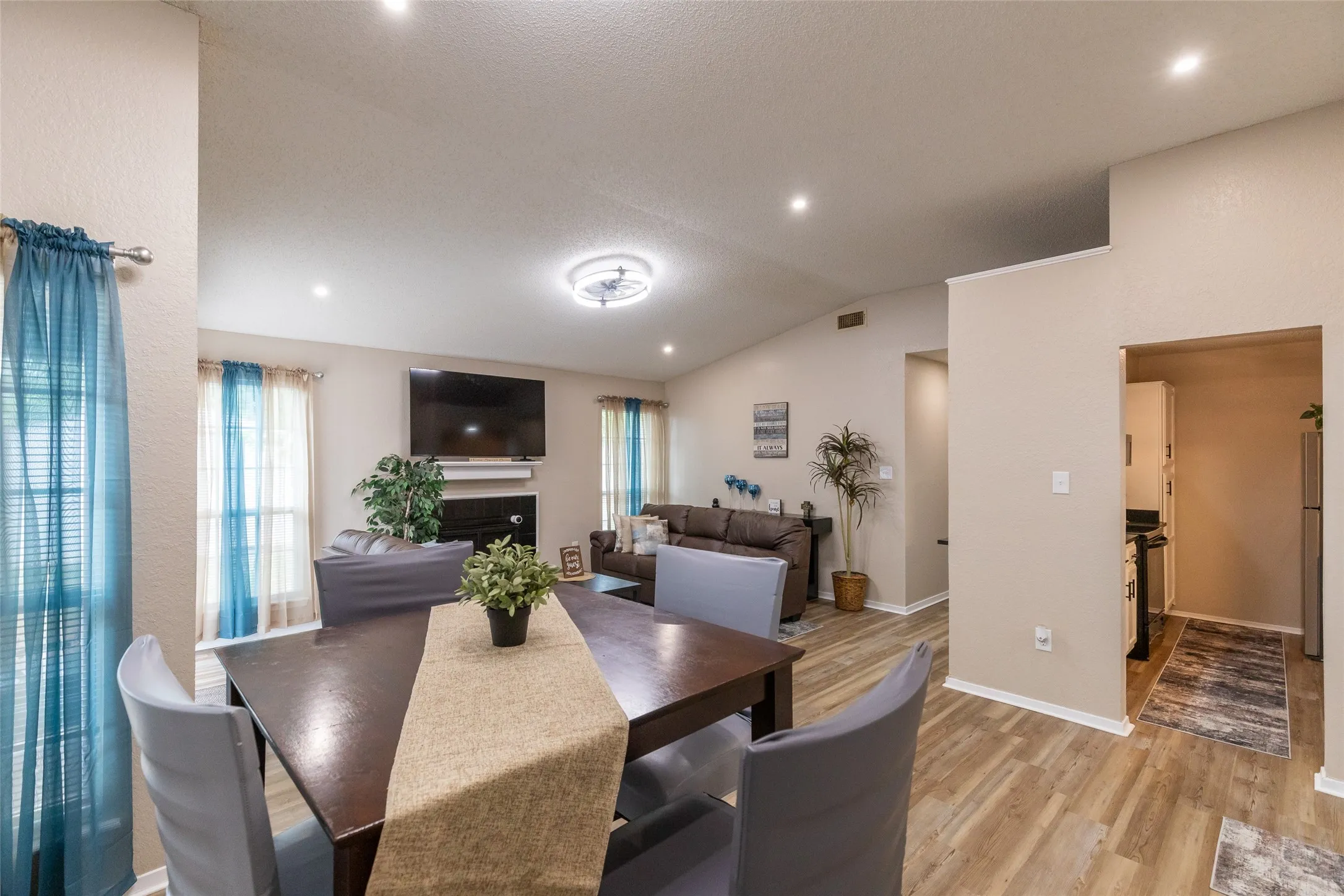 Open-concept interior featuring wood-finish flooring, vaulted ceilings, recessed lighting, and a fireplace with a mantel