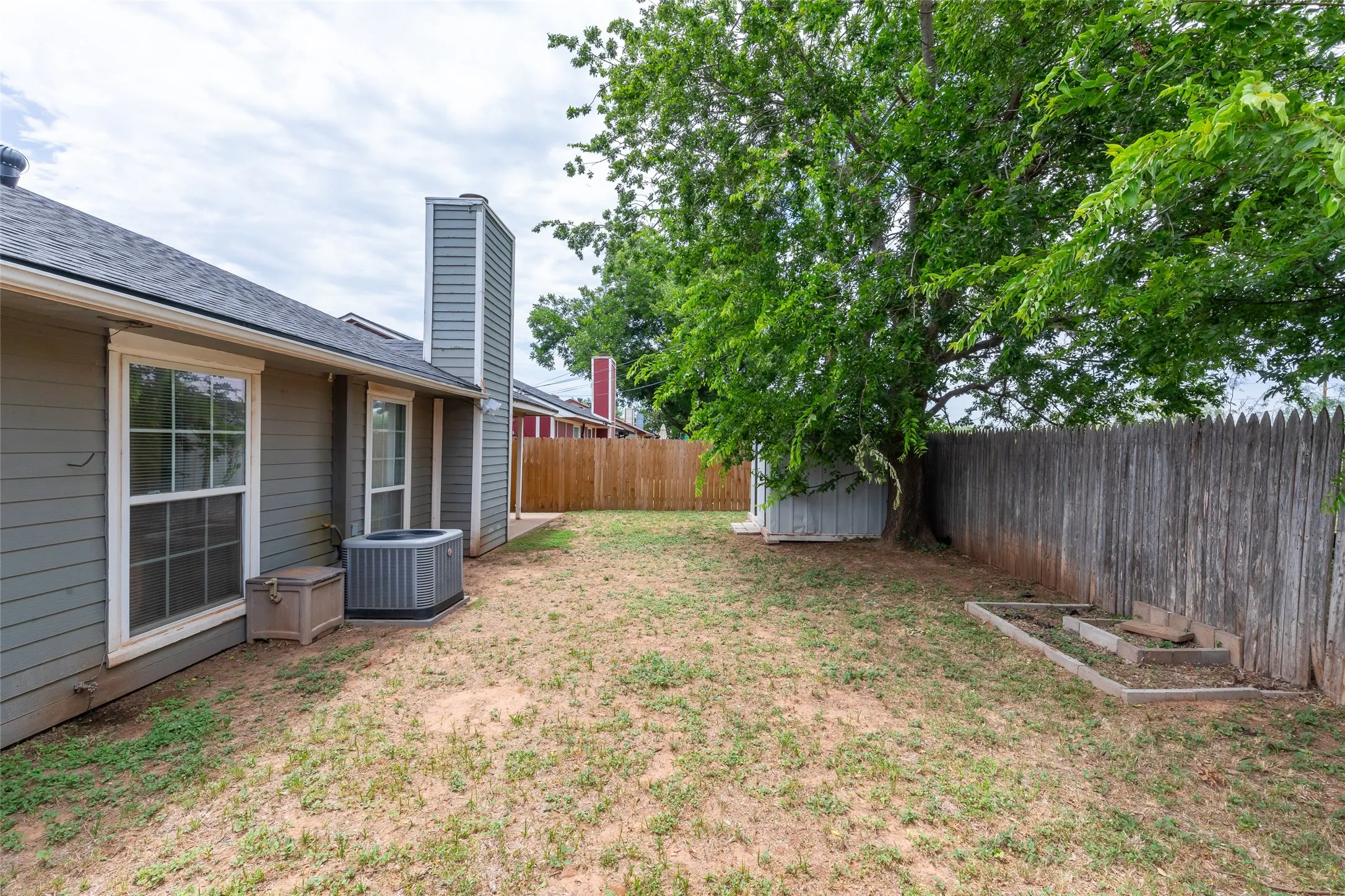 Fenced backyard featuring mature trees, wood fencing, and a built-in garden bed