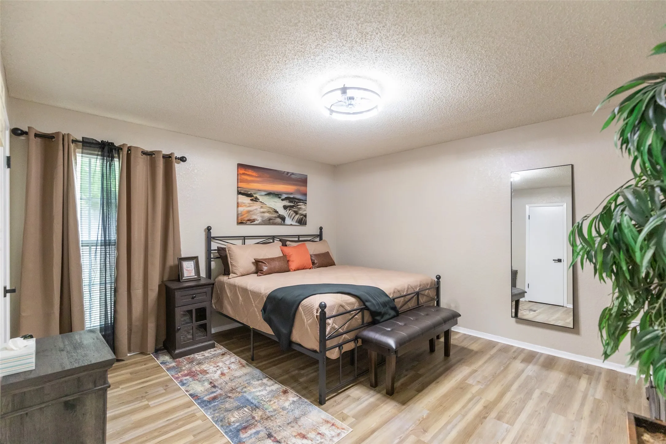 Spacious  Master bedroom featuring light wood-finish flooring and a contemporary ceiling light fixture