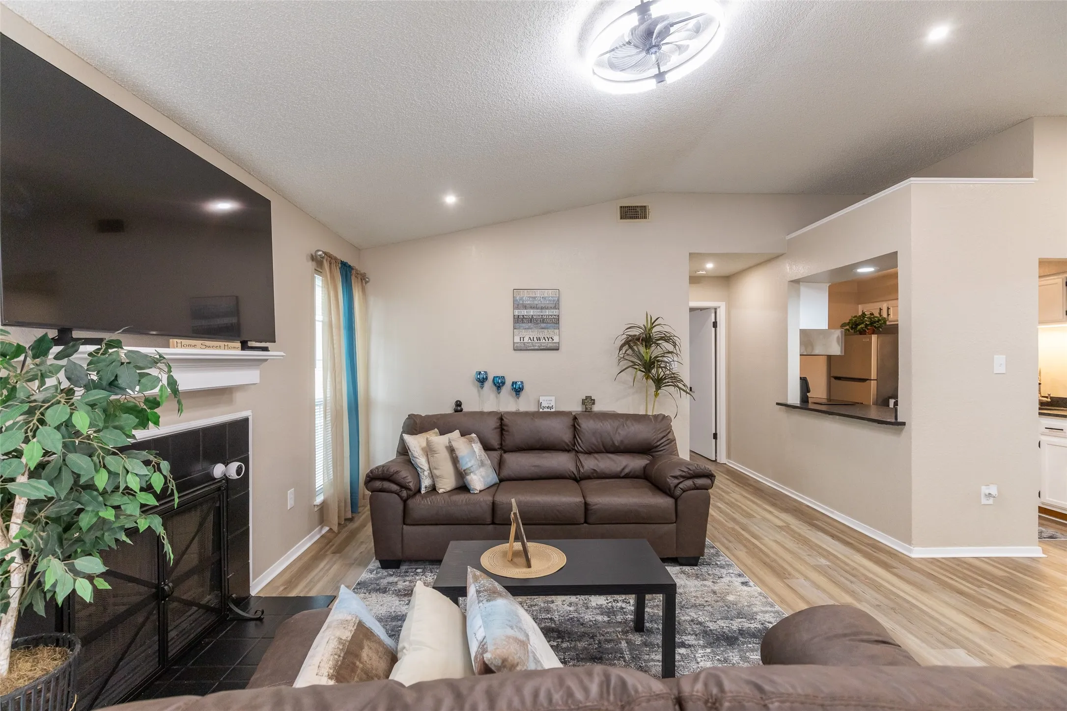 Vaulted ceilings highlight this living area featuring wood-finish flooring, recessed lighting, and a fireplace with a black tile surround and white mantel