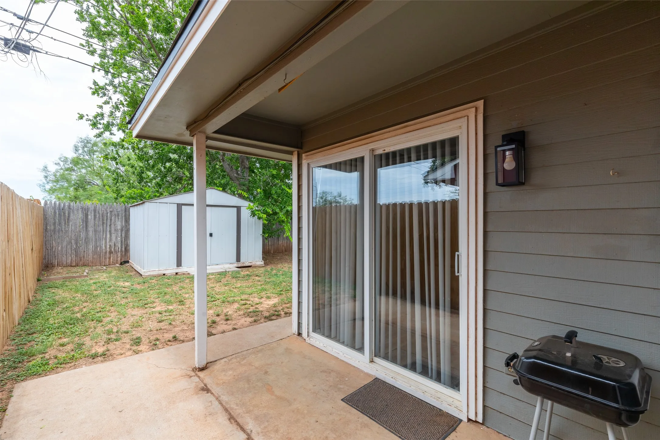 Patio area featuring a sliding glass door, overhead covering, and exterior wall sconce