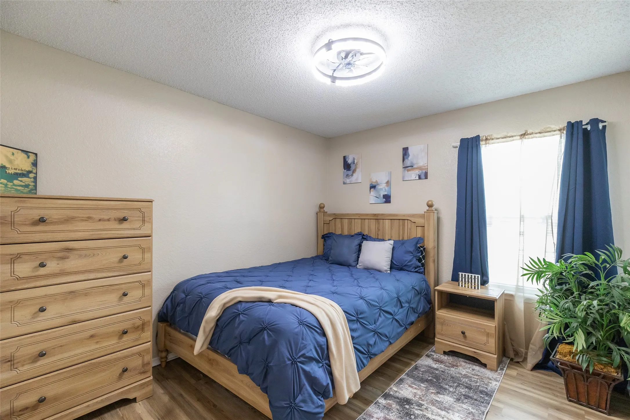 Bedroom 3  featuring light-toned walls, wood-finish flooring, a ceiling-mounted light fixture, and a window with curtains