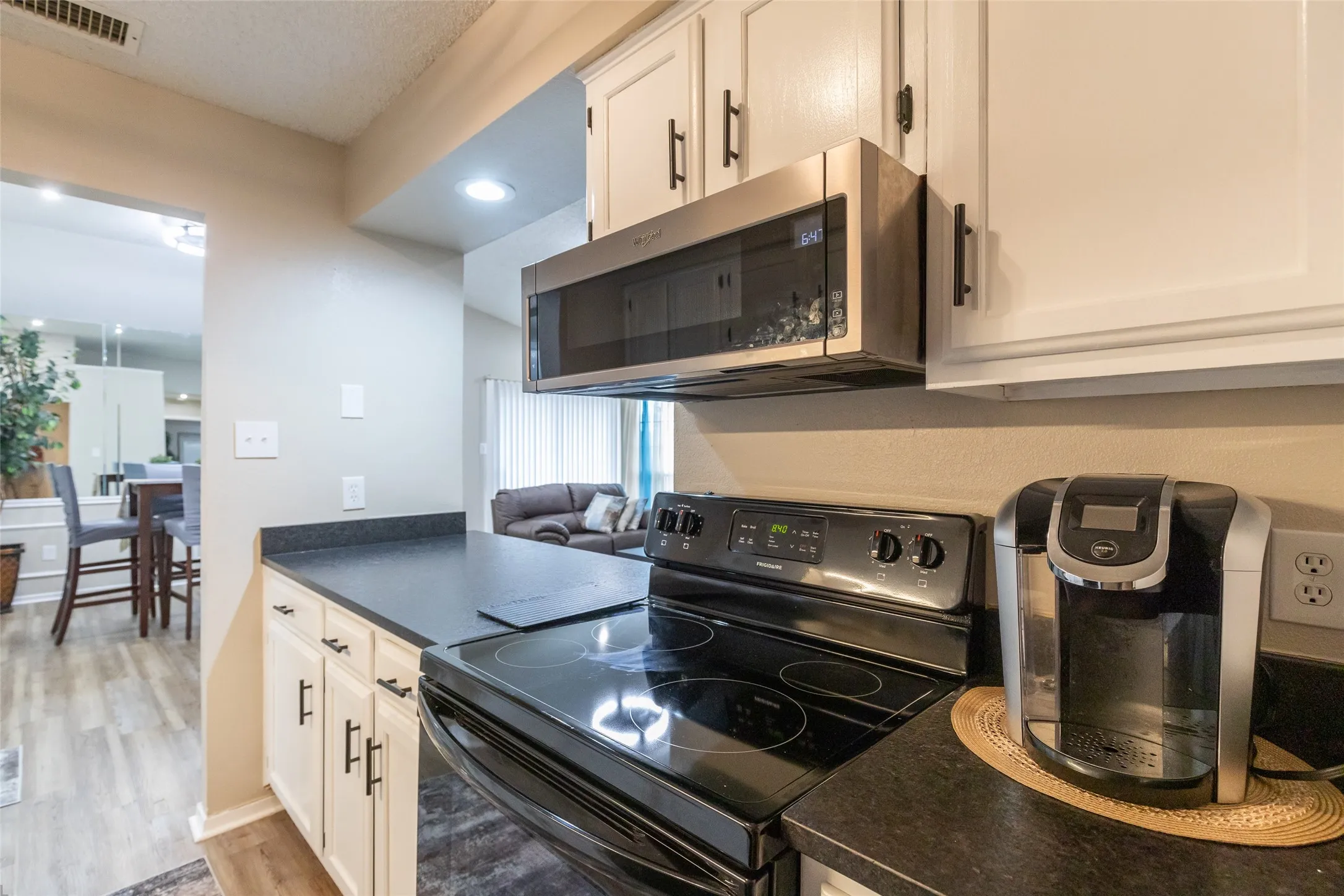 Kitchen featuring white cabinetry with black hardware, dark countertops, a black electric range, and a stainless steel over-the-range microwave