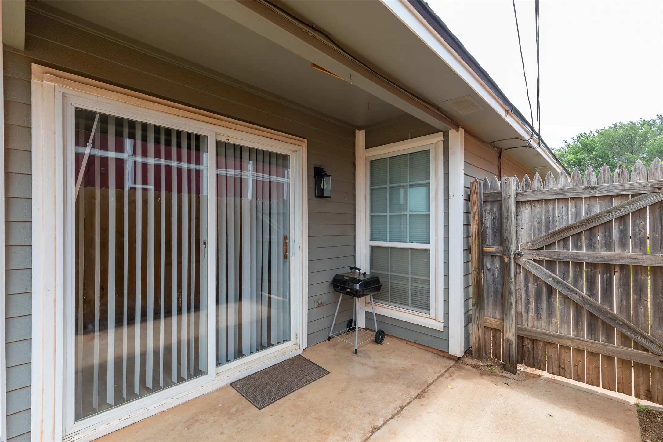 Private concrete patio featuring a sliding glass door entry, a single window, exterior siding, and a wooden privacy fence