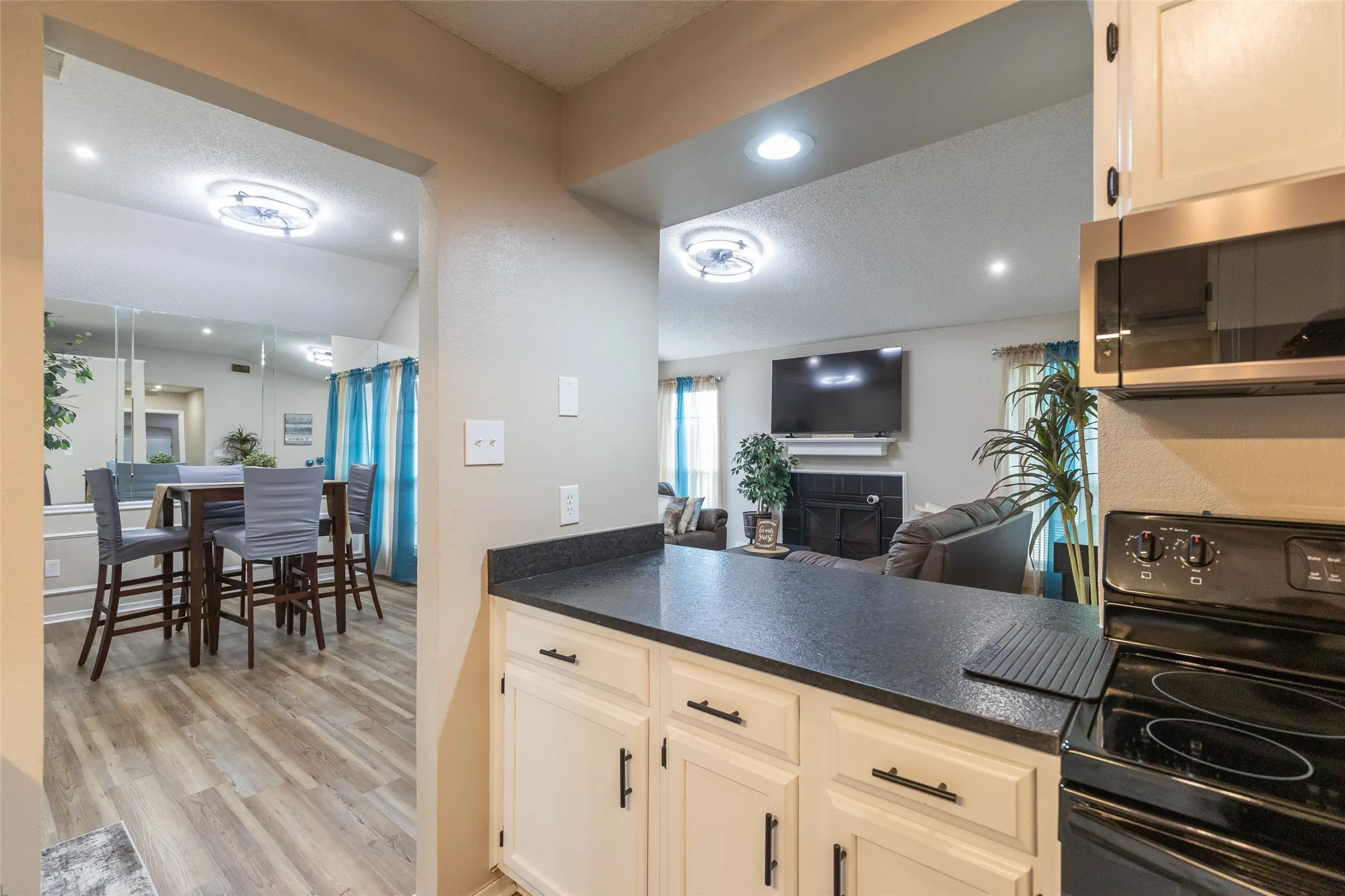 Kitchen counter bar with white cabinetry, dark countertops, and stainless steel microwave