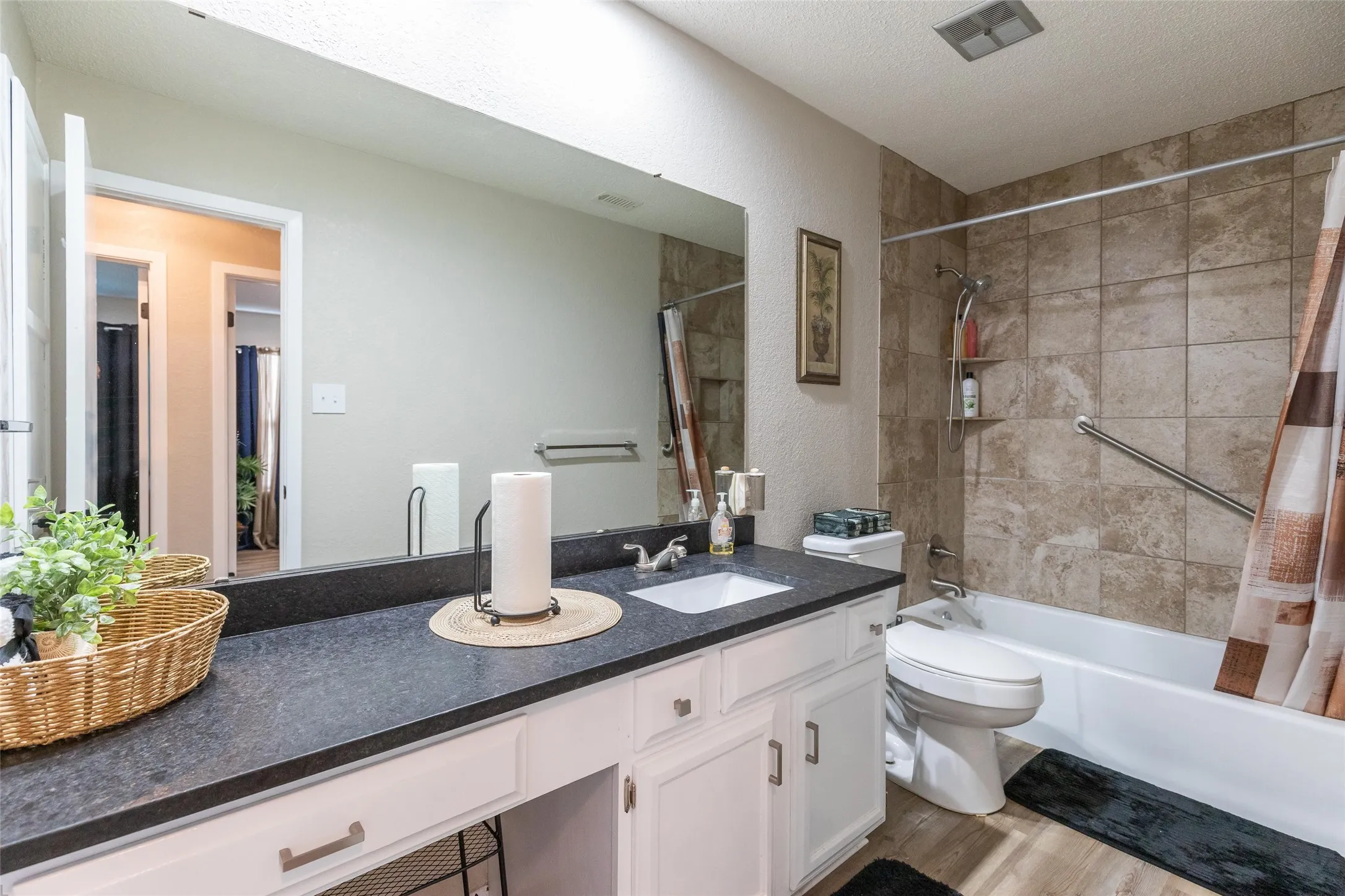 Bathroom 2  featuring a spacious vanity with a dark countertop and integrated sink, white cabinetry, a large wall-mounted mirror, a tiled shower/tub combination, and wood-finish flooring
