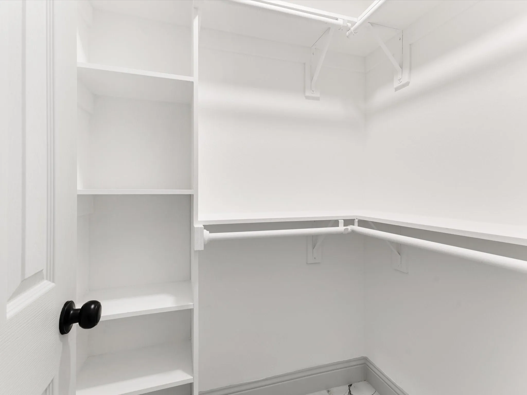 White walk-in closet featuring extensive built-in shelving, multiple hanging rods, and a white paneled door with a matte black knob
