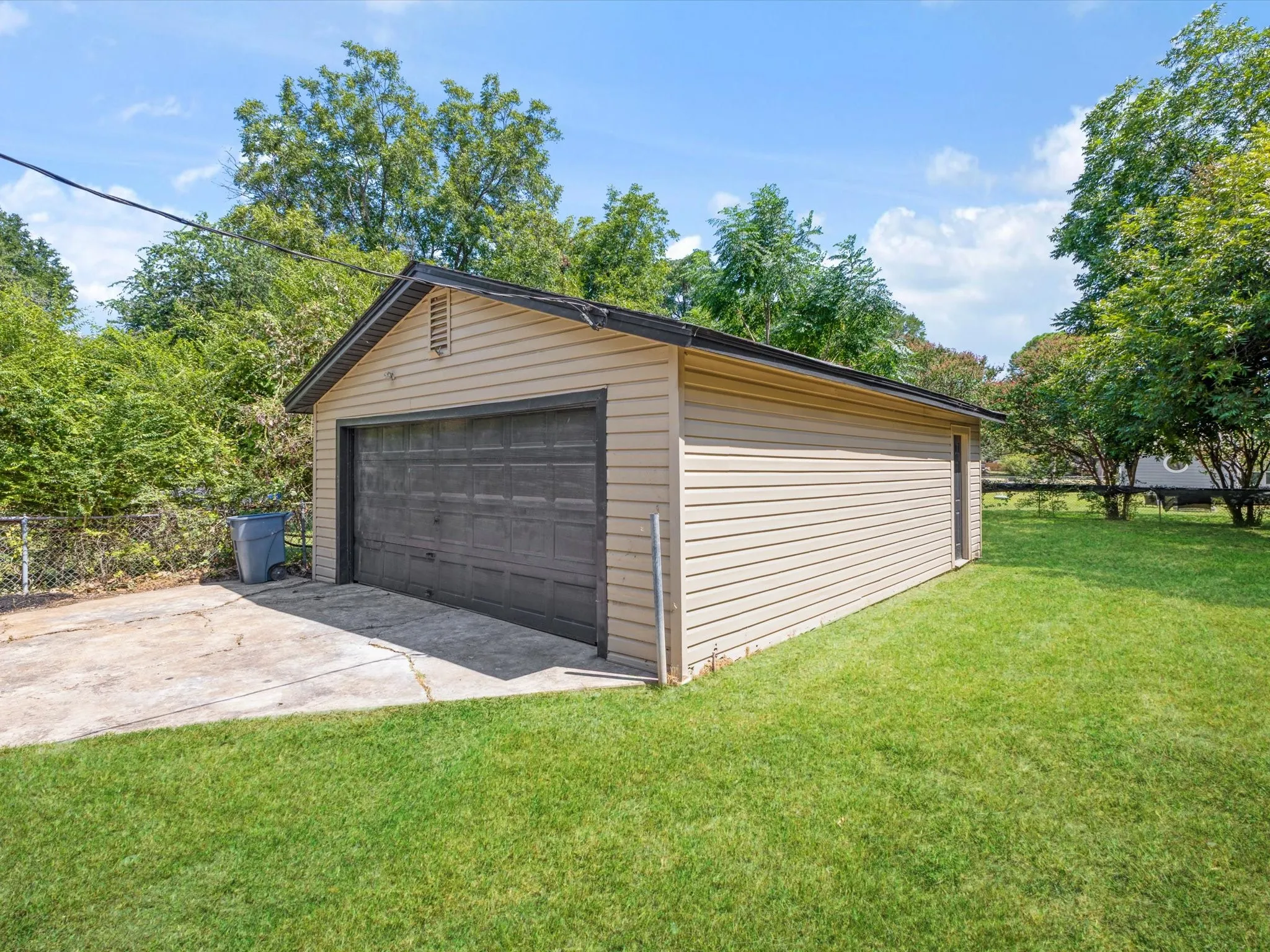 Detached two-car garage with beige vinyl siding, a dark paneled garage door, and a gable roof with dark shingles