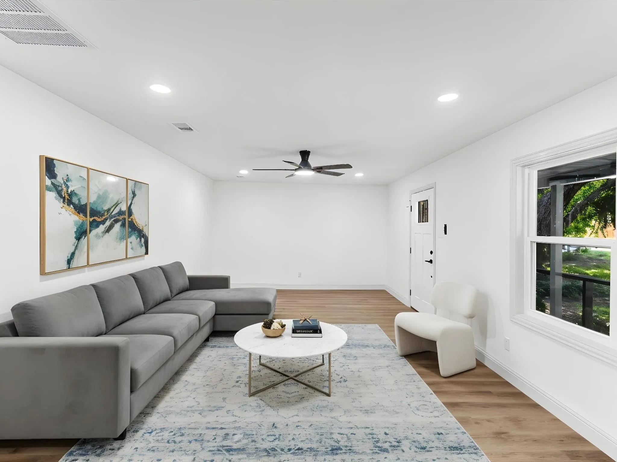 Spacious living area featuring wood-finish flooring, recessed lighting, and a ceiling fan- AI Staged