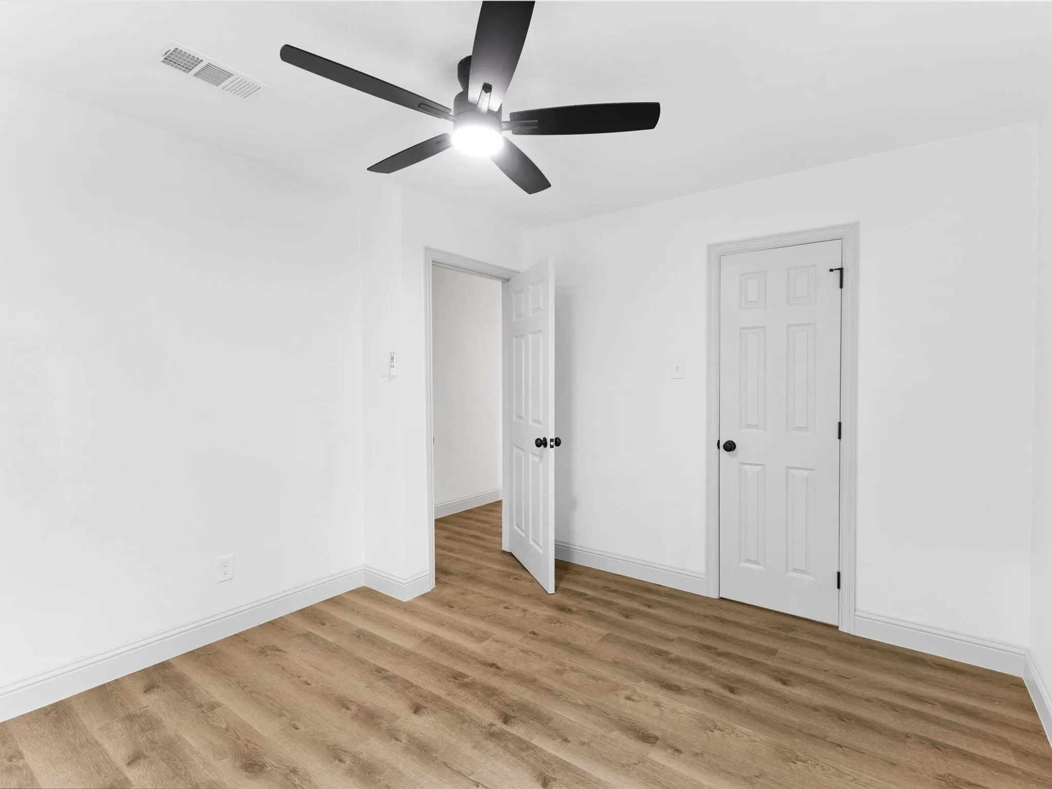 Bedroom featuring wood-finish flooring, white baseboards, a ceiling fan with integrated lighting, a panel door with matte black hardware, and an open doorway