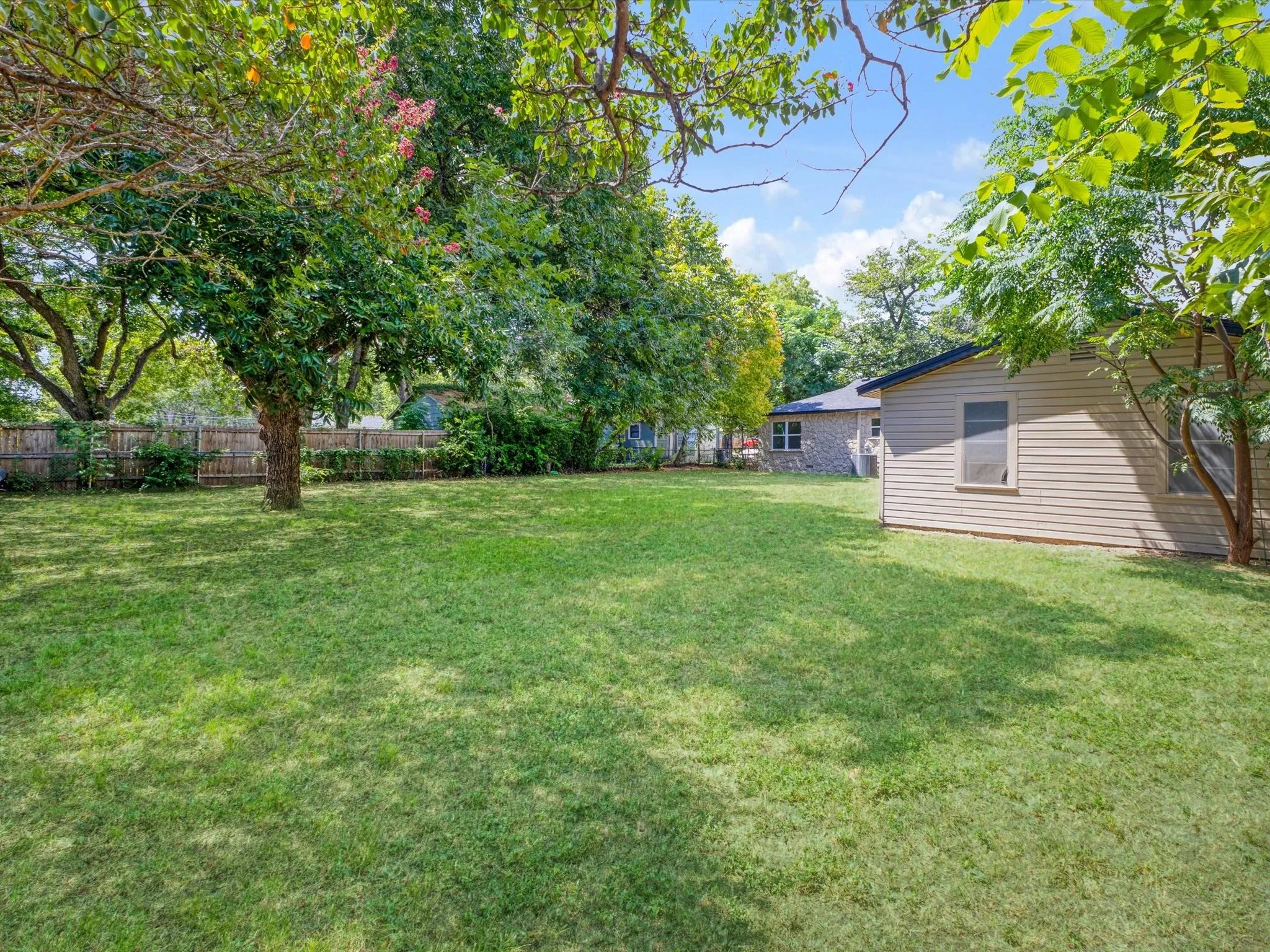 Spacious backyard featuring a manicured lawn, established shade trees, and a wood privacy fence
