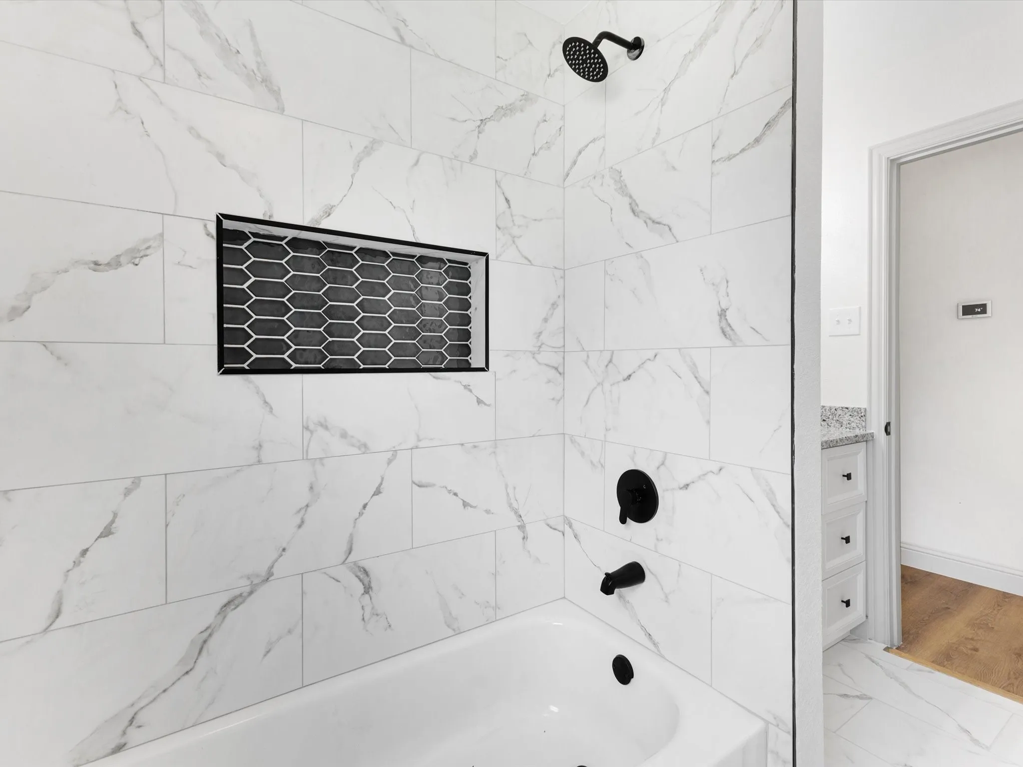 Bathtub and shower combination featuring large format white tile with grey veining