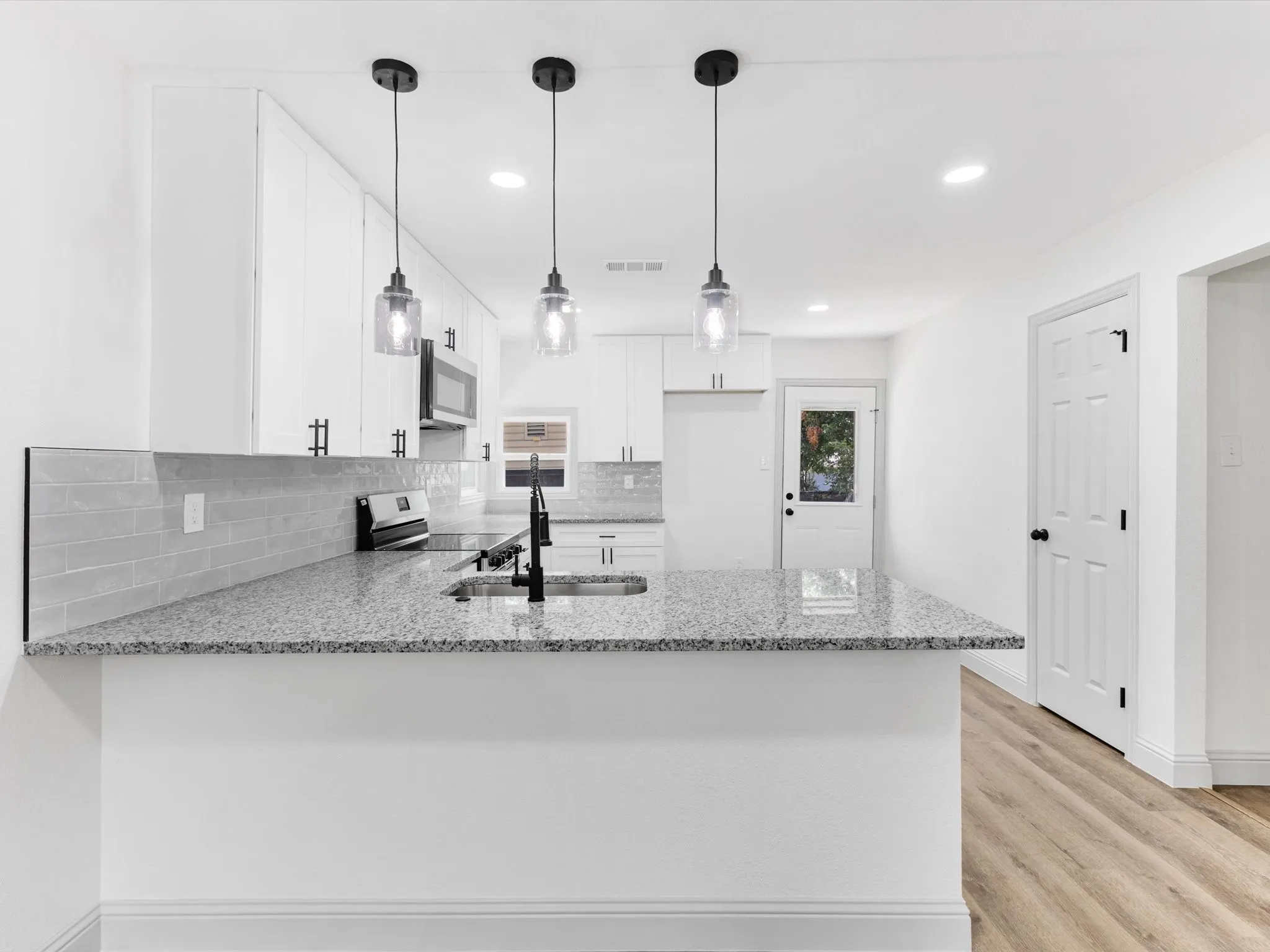 Modern kitchen featuring a peninsula with granite countertops, three pendant lights, and a matte black faucet