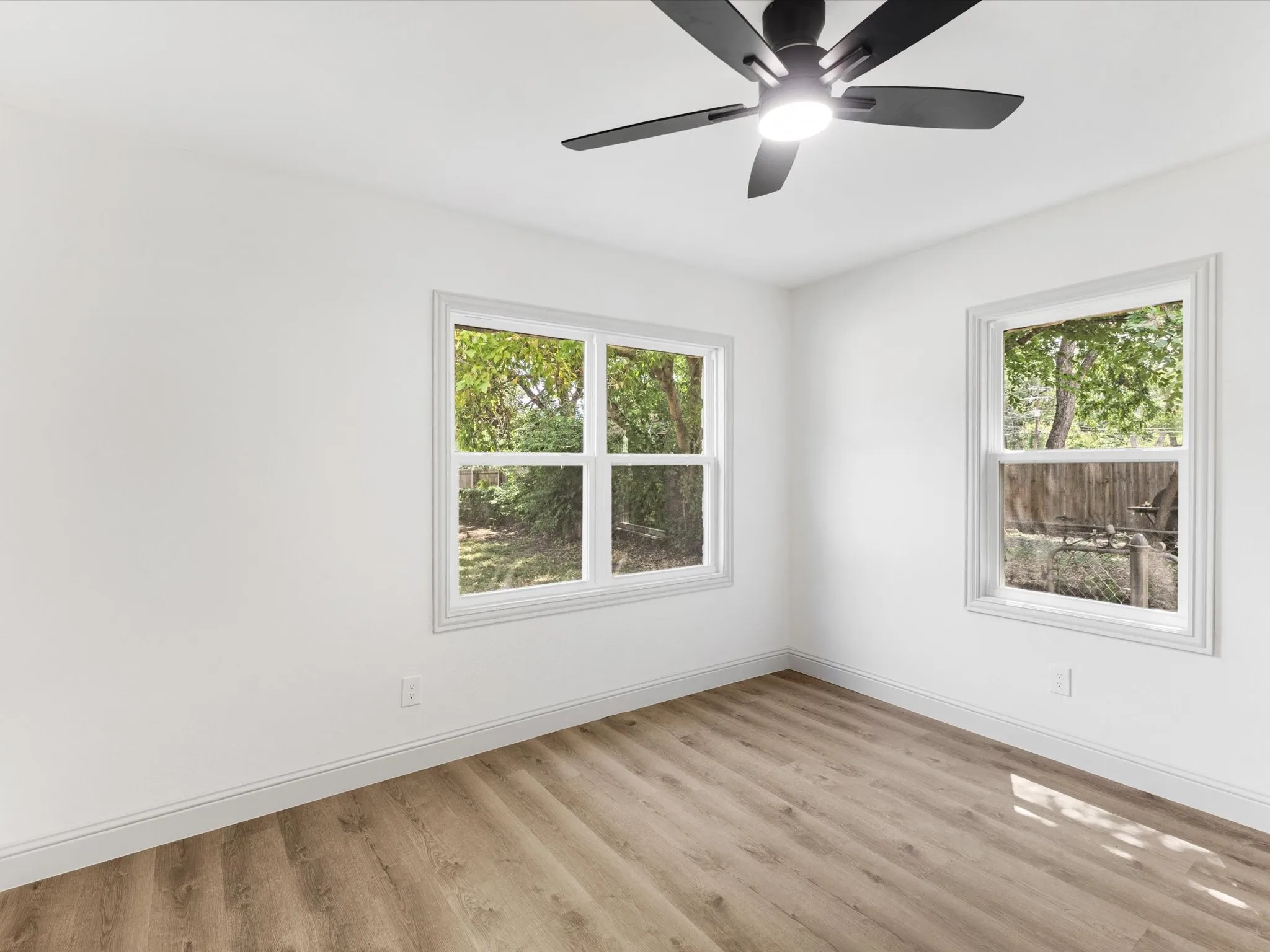 Bright interior room featuring wood-finish flooring, white baseboards, and a contemporary black ceiling fan with integrated lighting