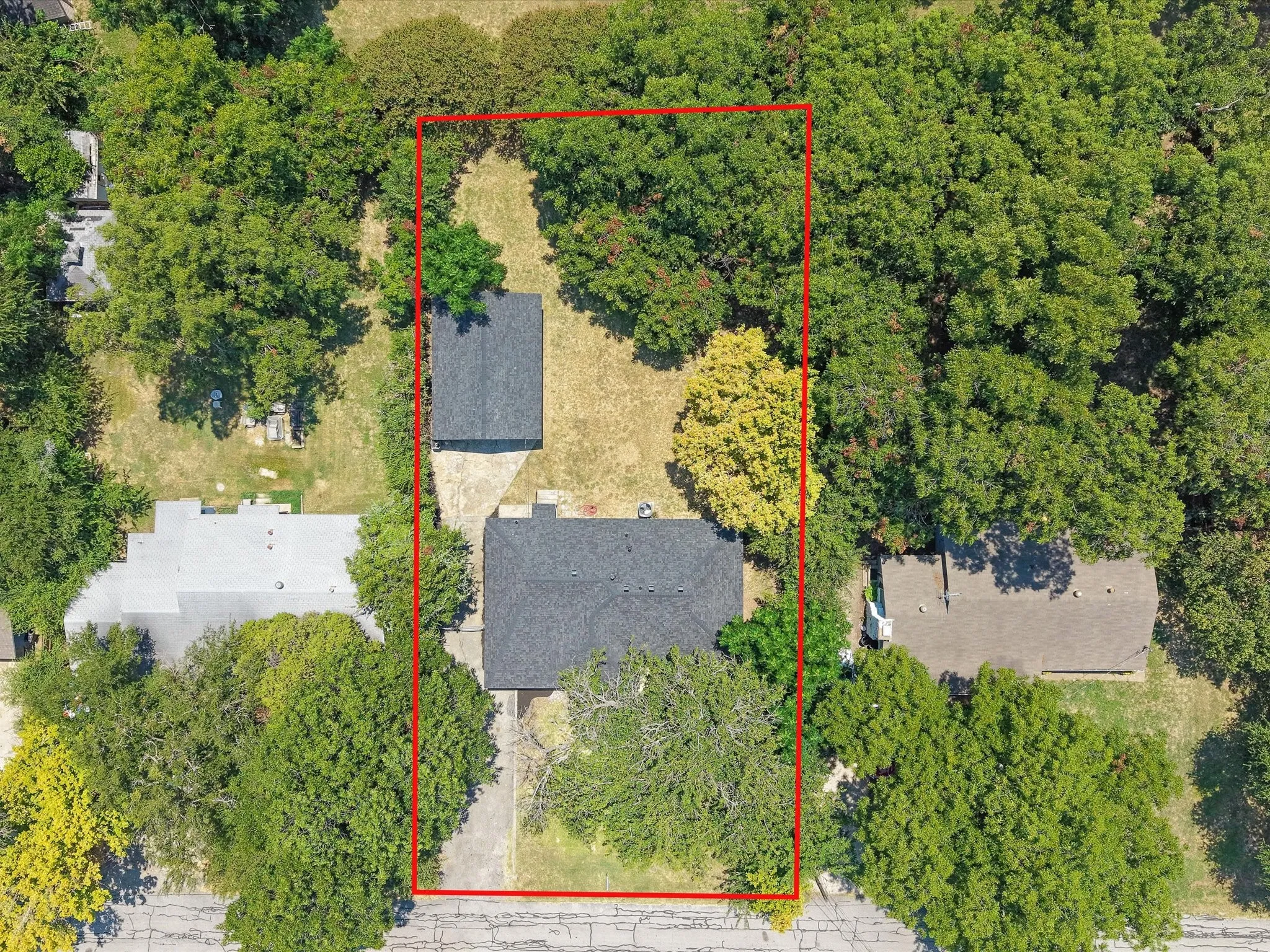 Aerial view of the property with a main residence and an additional detached structure, surrounded by mature trees