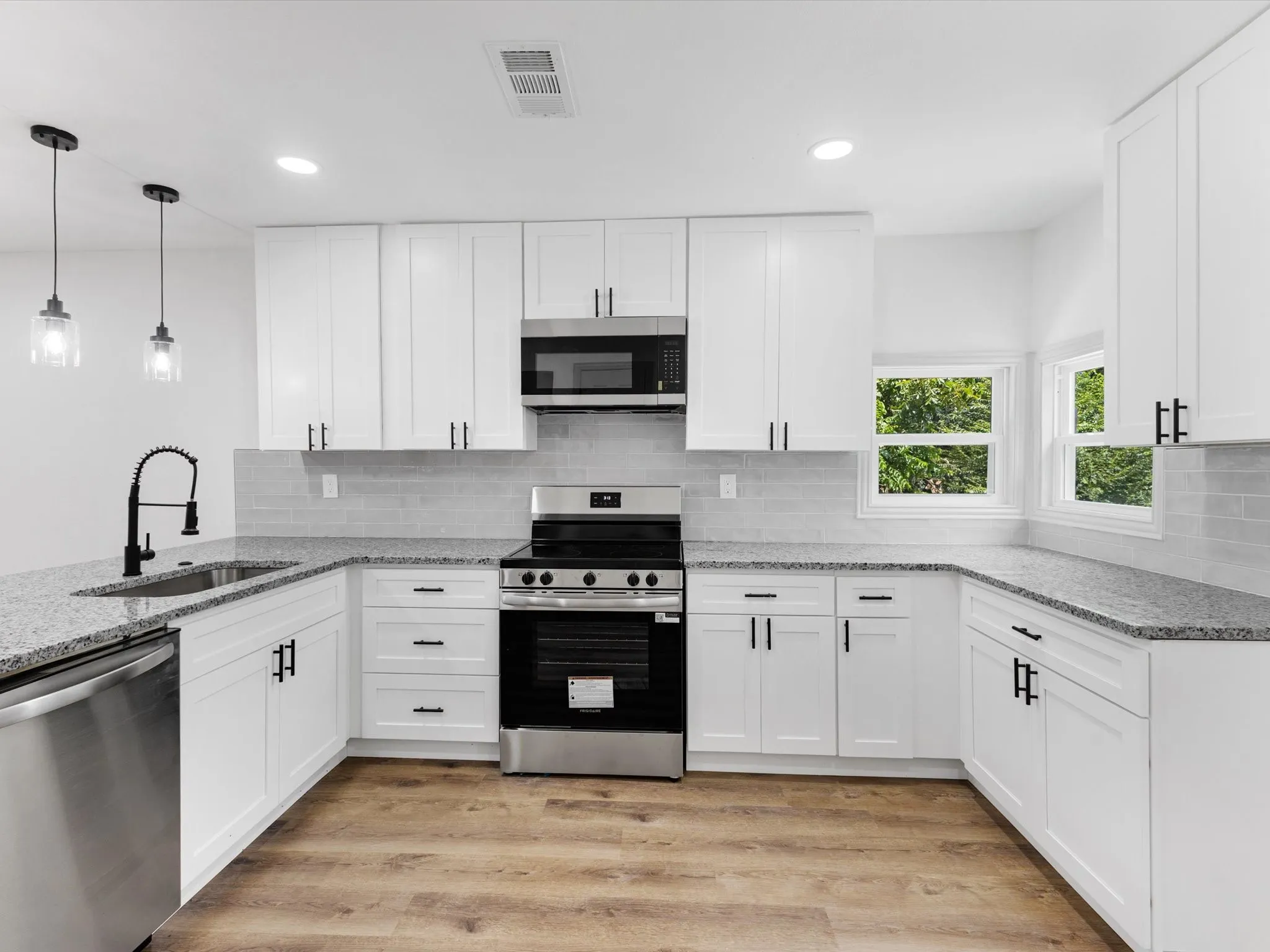 Contemporary kitchen featuring white cabinetry with black hardware, stainless steel appliances, granite countertops, and wood-finish flooring