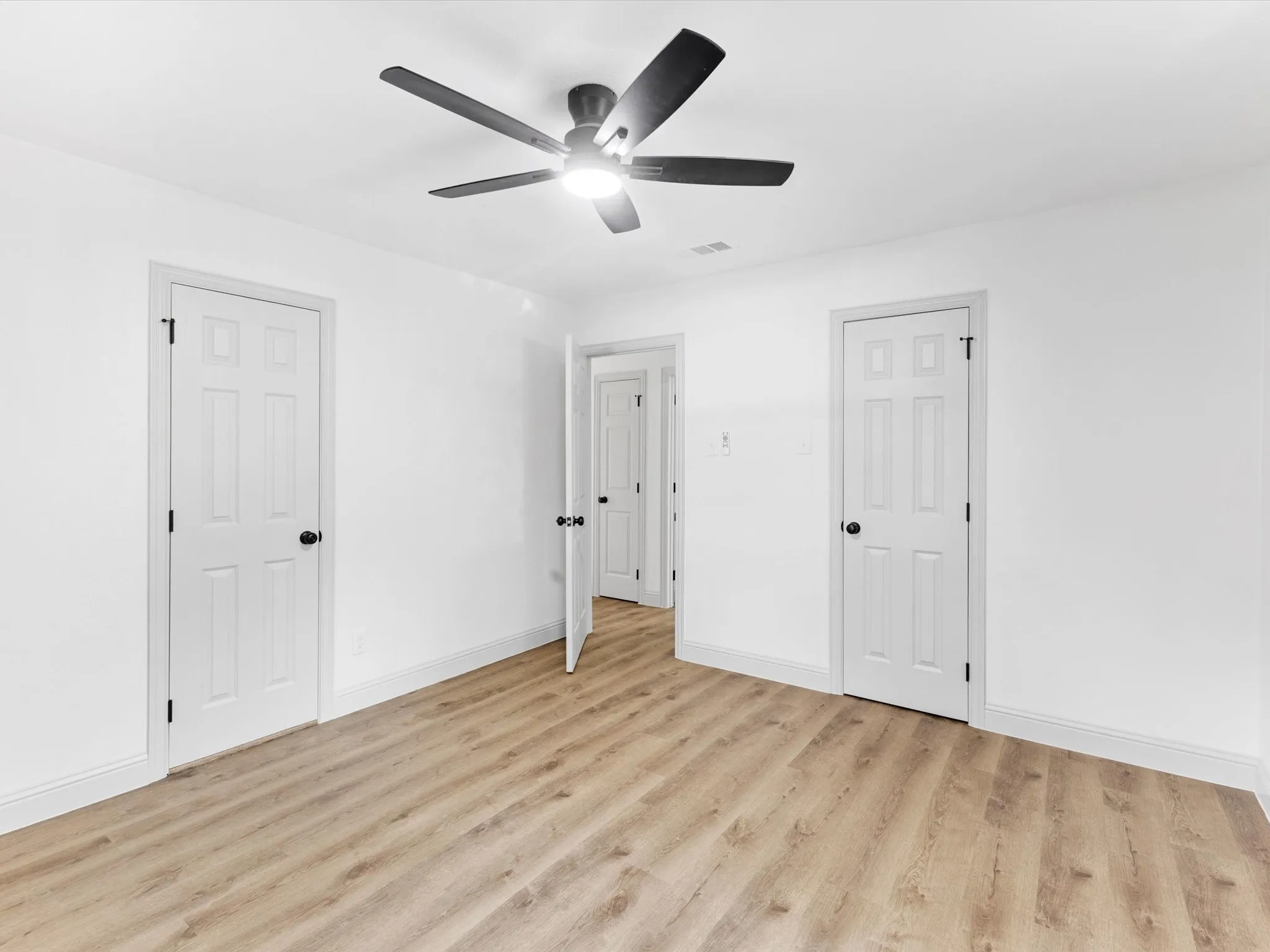 Room featuring wood-finish flooring, white walls, and a ceiling fan with integrated lighting