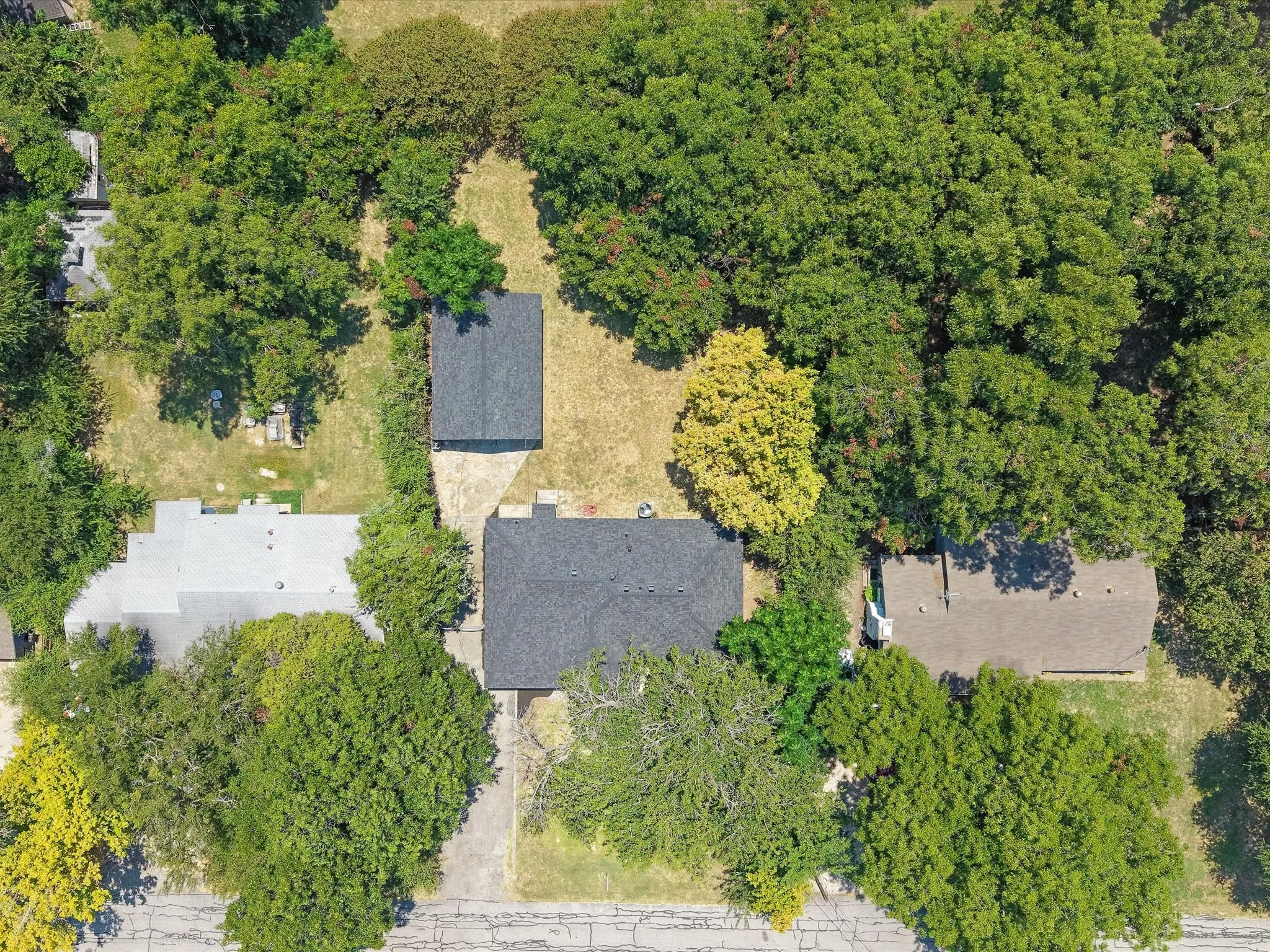 Property featuring a primary dwelling with a dark shingle roof, a secondary structure with a dark shingle roof, and established trees throughout the grounds