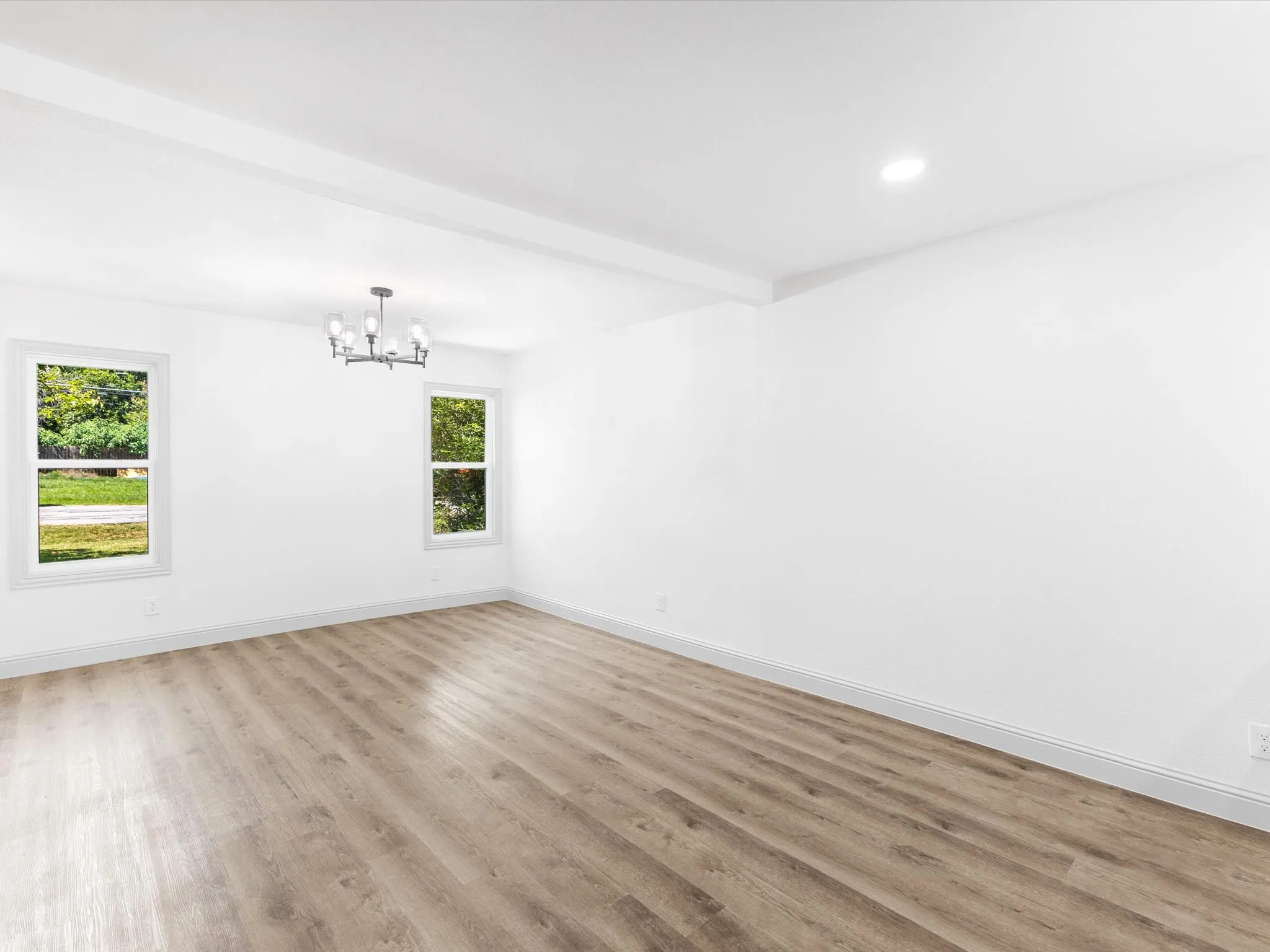 Spacious room featuring wood-finish flooring, white walls, two windows, and a ceiling-mounted light fixture