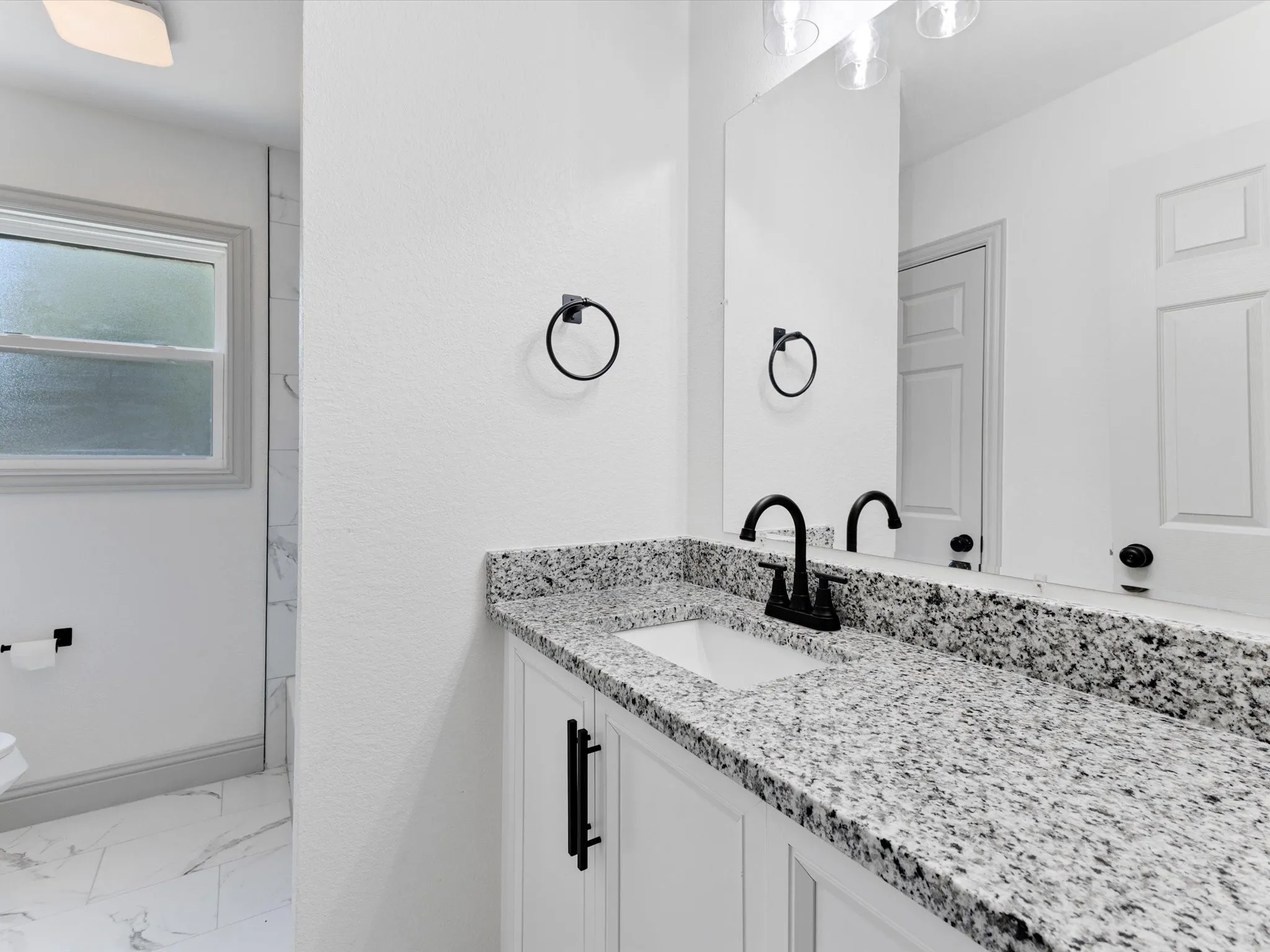 Bathroom vanity featuring a speckled countertop, integrated white sink, and matte black faucet