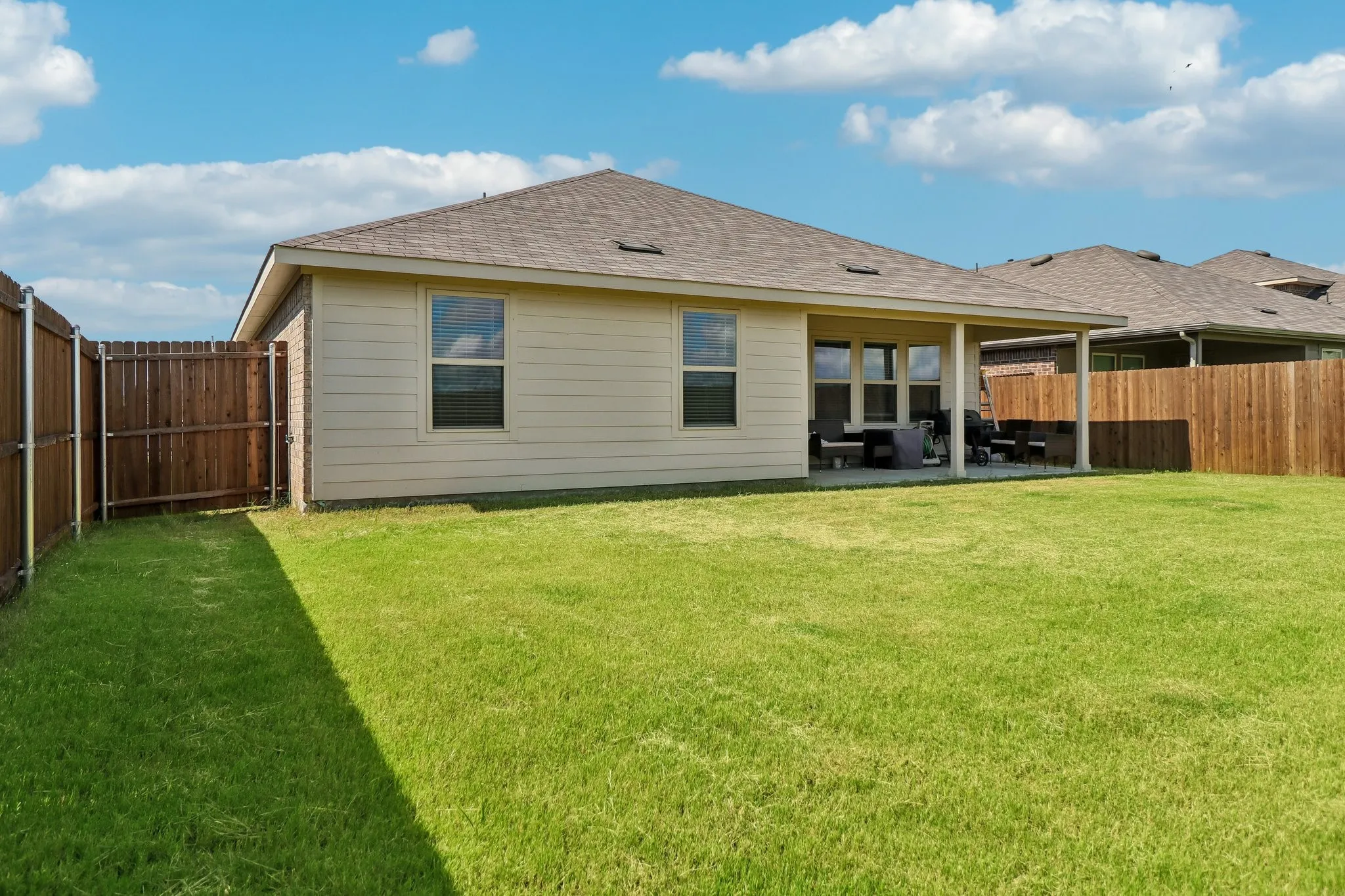 Expansive backyard featuring a manicured lawn, full wood privacy fencing, and a covered patio