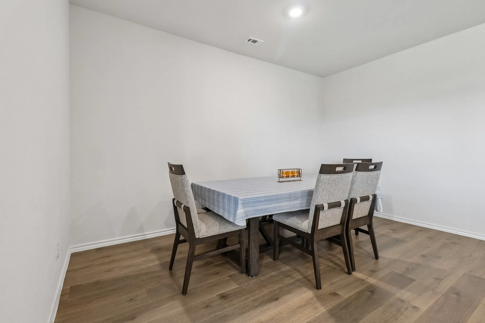 Spacious room featuring light-toned walls, wood-finish flooring, and recessed ceiling lighting