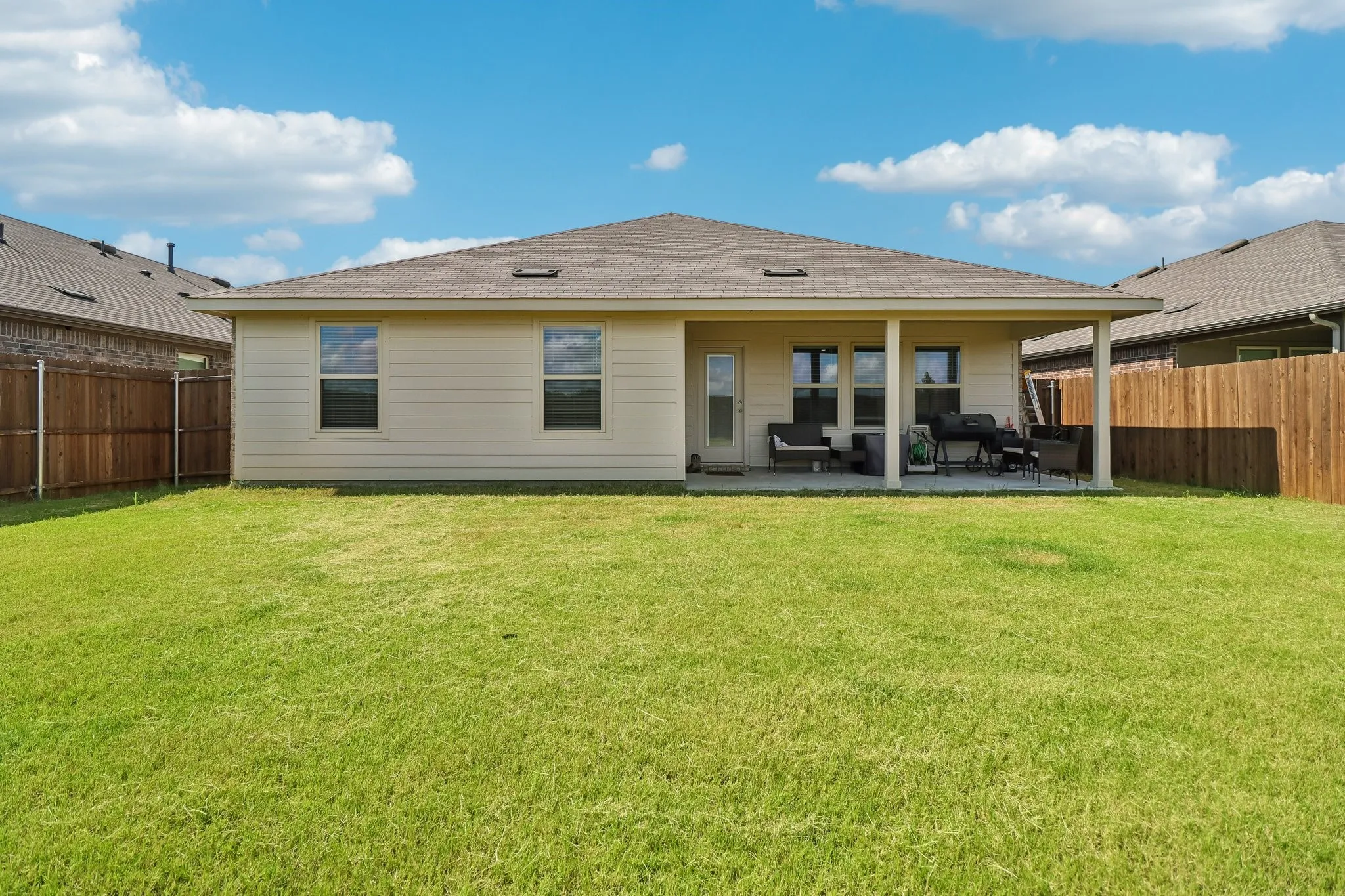 Expansive backyard featuring a covered patio, neutral siding, a brown shingle roof, and wood fencing