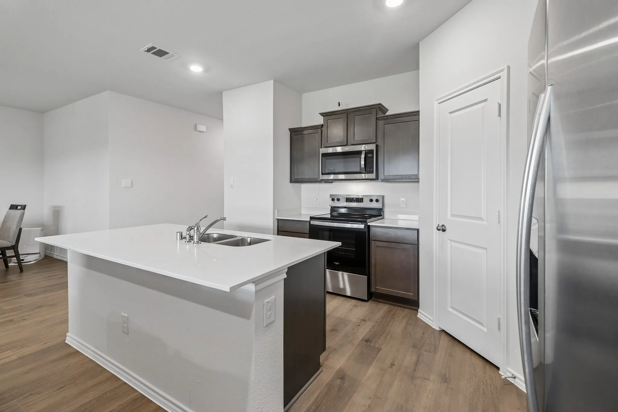 Kitchen featuring a central island with dual basin sink, white countertops, dark wood cabinetry, stainless steel appliances, and wood-finish flooring