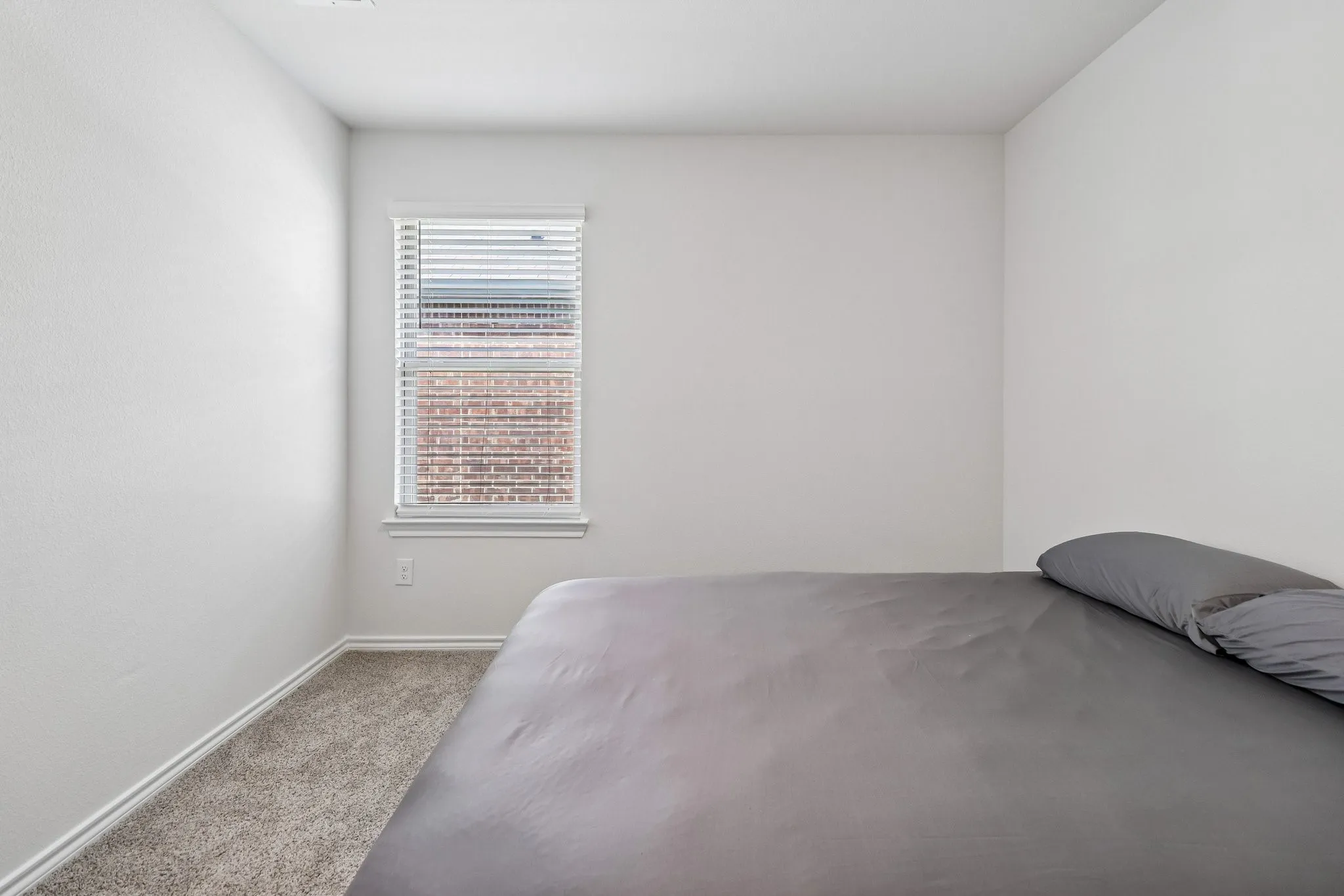 Light-filled room featuring a single window with blinds, neutral wall paint, white baseboards, and soft carpet flooring