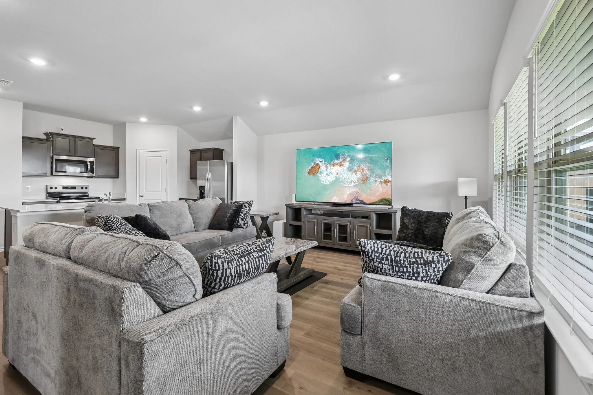 Open-concept living area with wood-finish flooring, recessed lighting, and multiple windows with horizontal blinds
