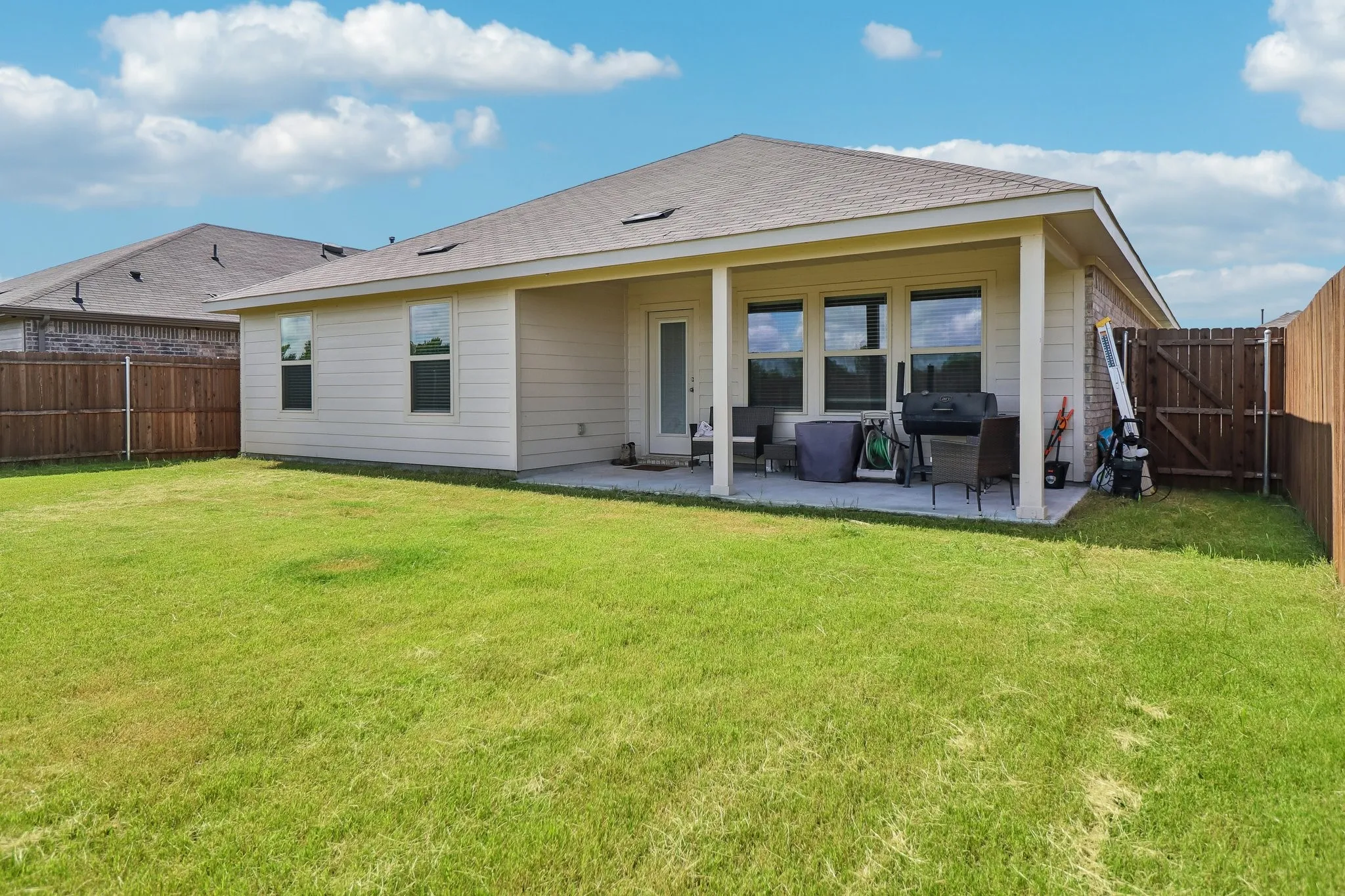 Expansive backyard featuring a covered patio, multiple windows, a rear entry door, and wood fencing