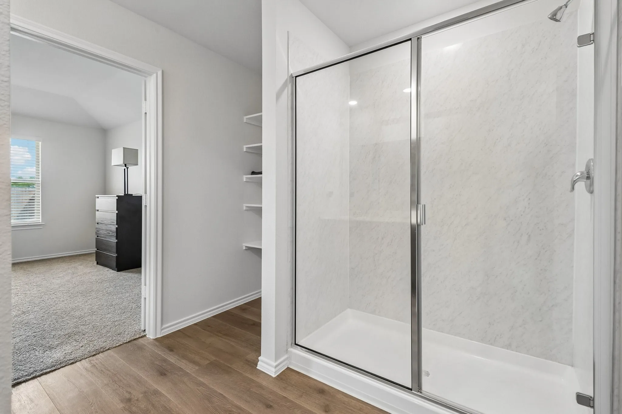 Walk-in shower with a glass enclosure and textured white surround