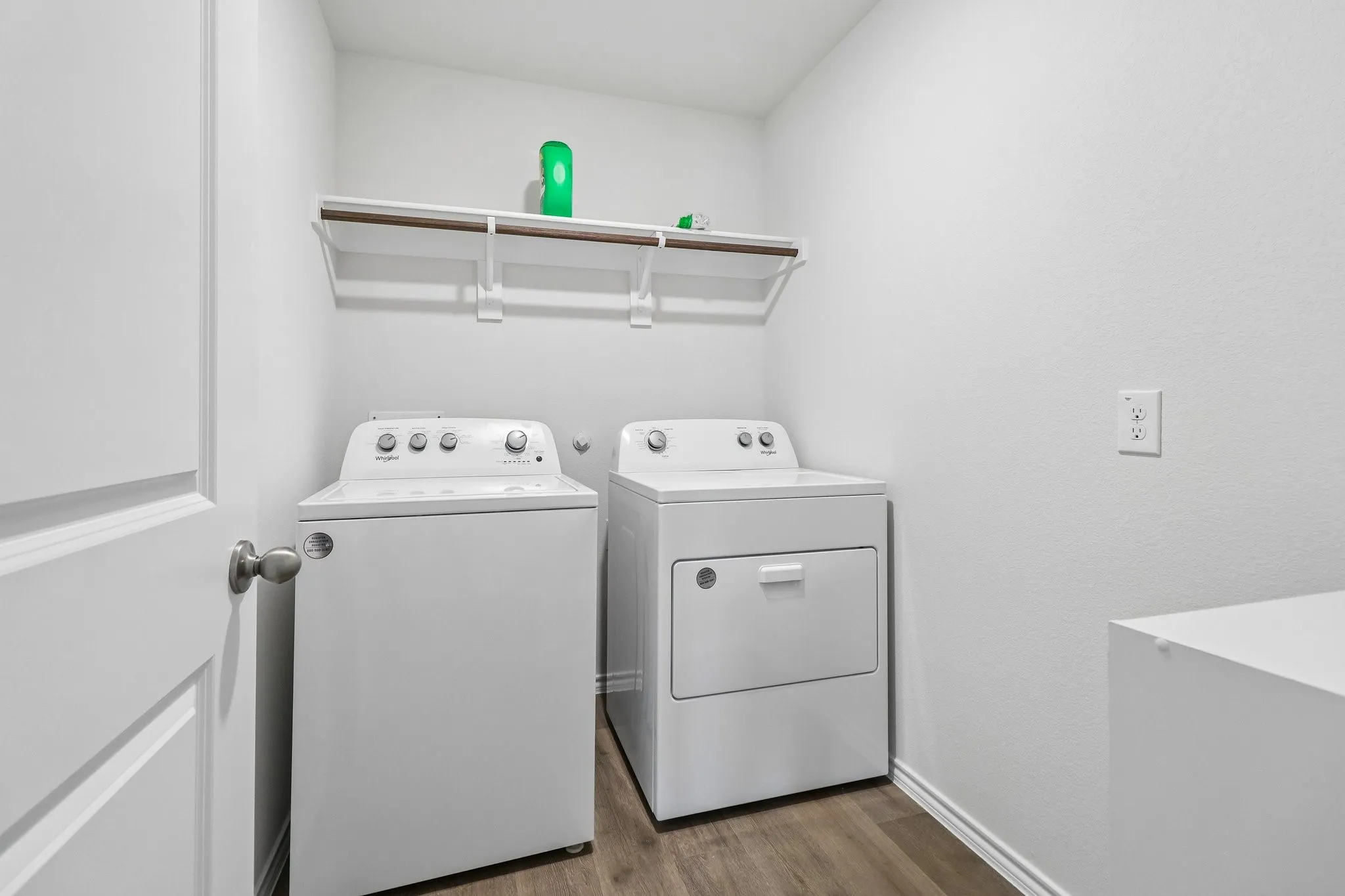 Dedicated laundry area featuring wood-finish flooring, white walls, and a built-in storage shelf with hanging rod