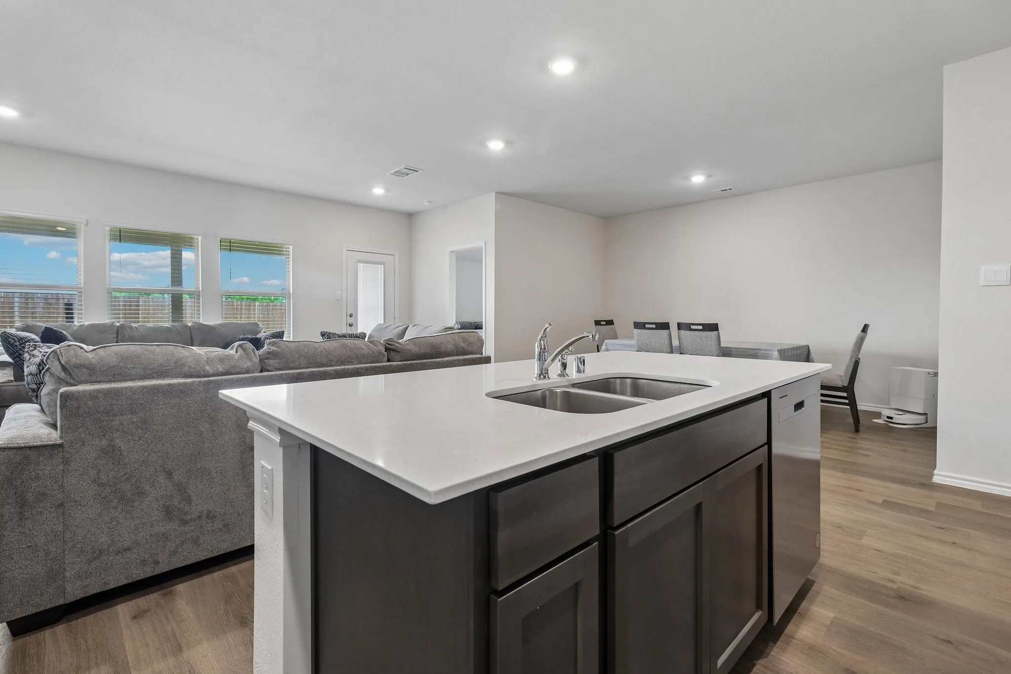Kitchen island featuring a dual-basin stainless steel sink, a chrome faucet, dark wood-finish cabinetry, and a light-toned countertop