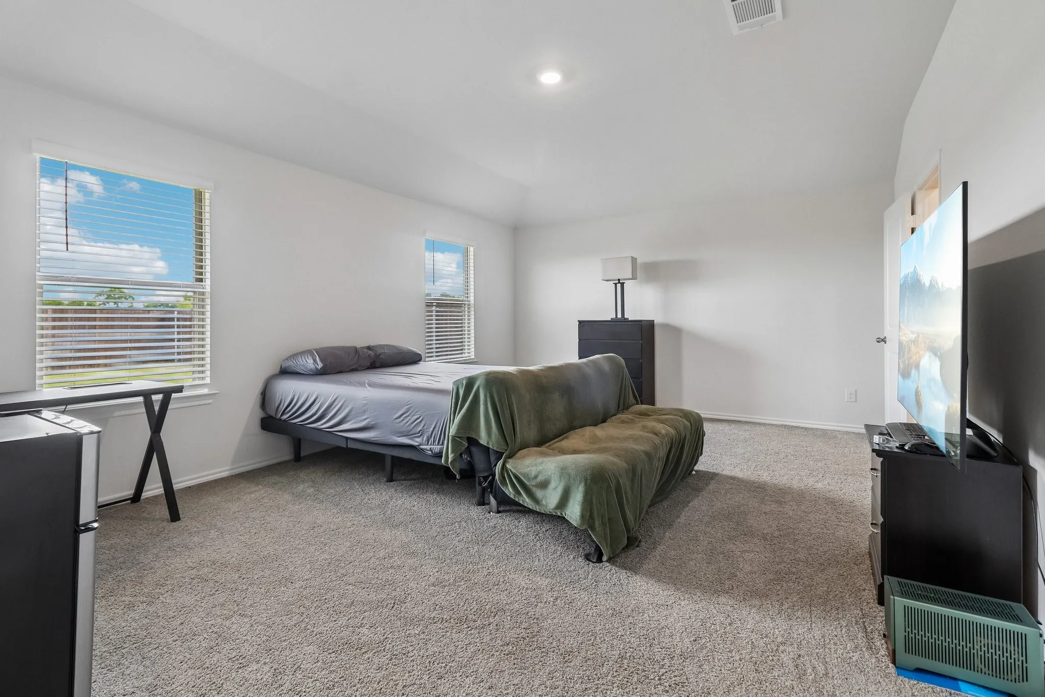 Carpeted room featuring two windows with horizontal blinds, white walls, and a vaulted ceiling