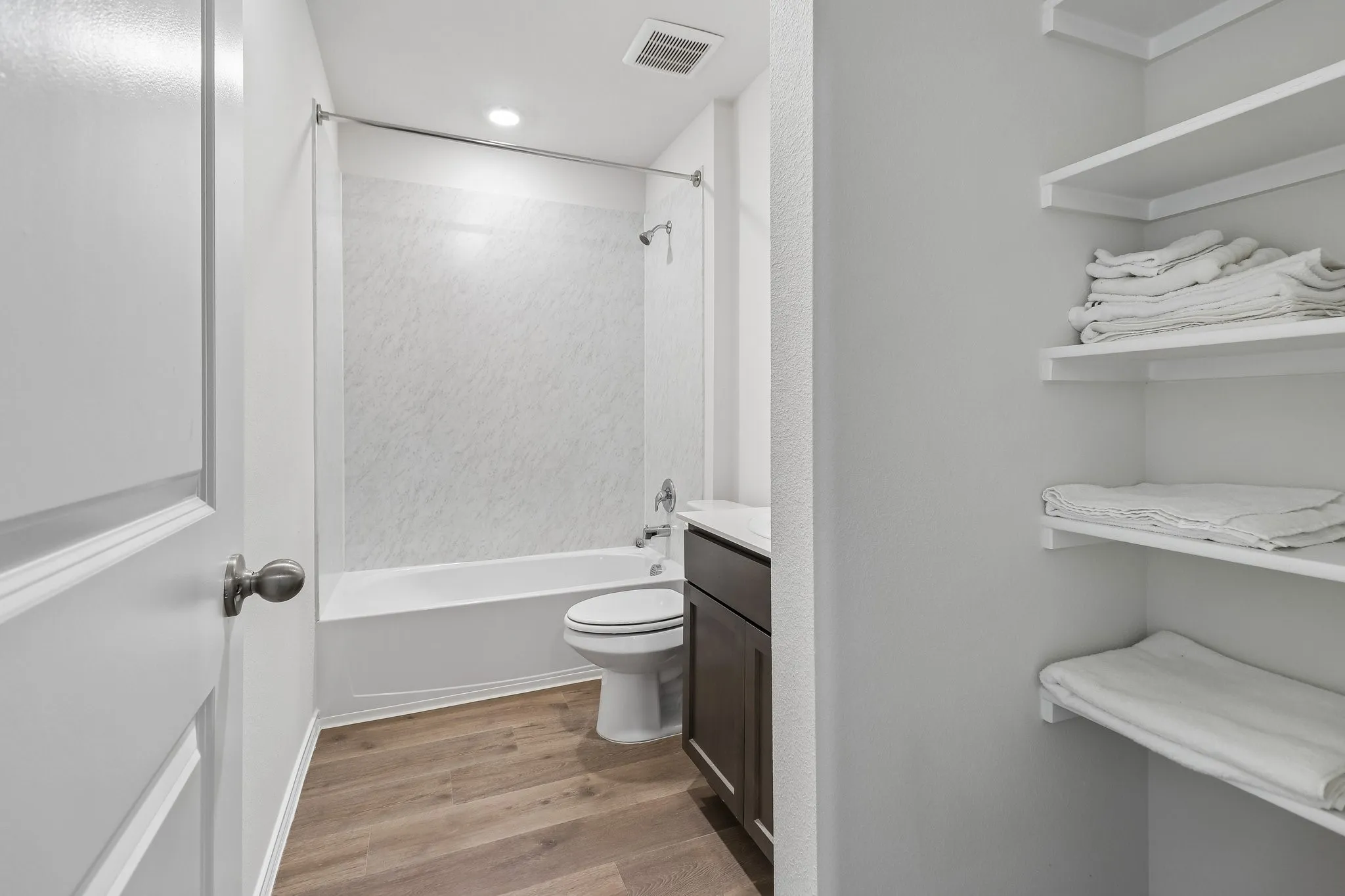 Bathroom featuring wood-finish flooring, a white bathtub, a single vanity with a dark wood cabinet and white countertop, and built-in shelving