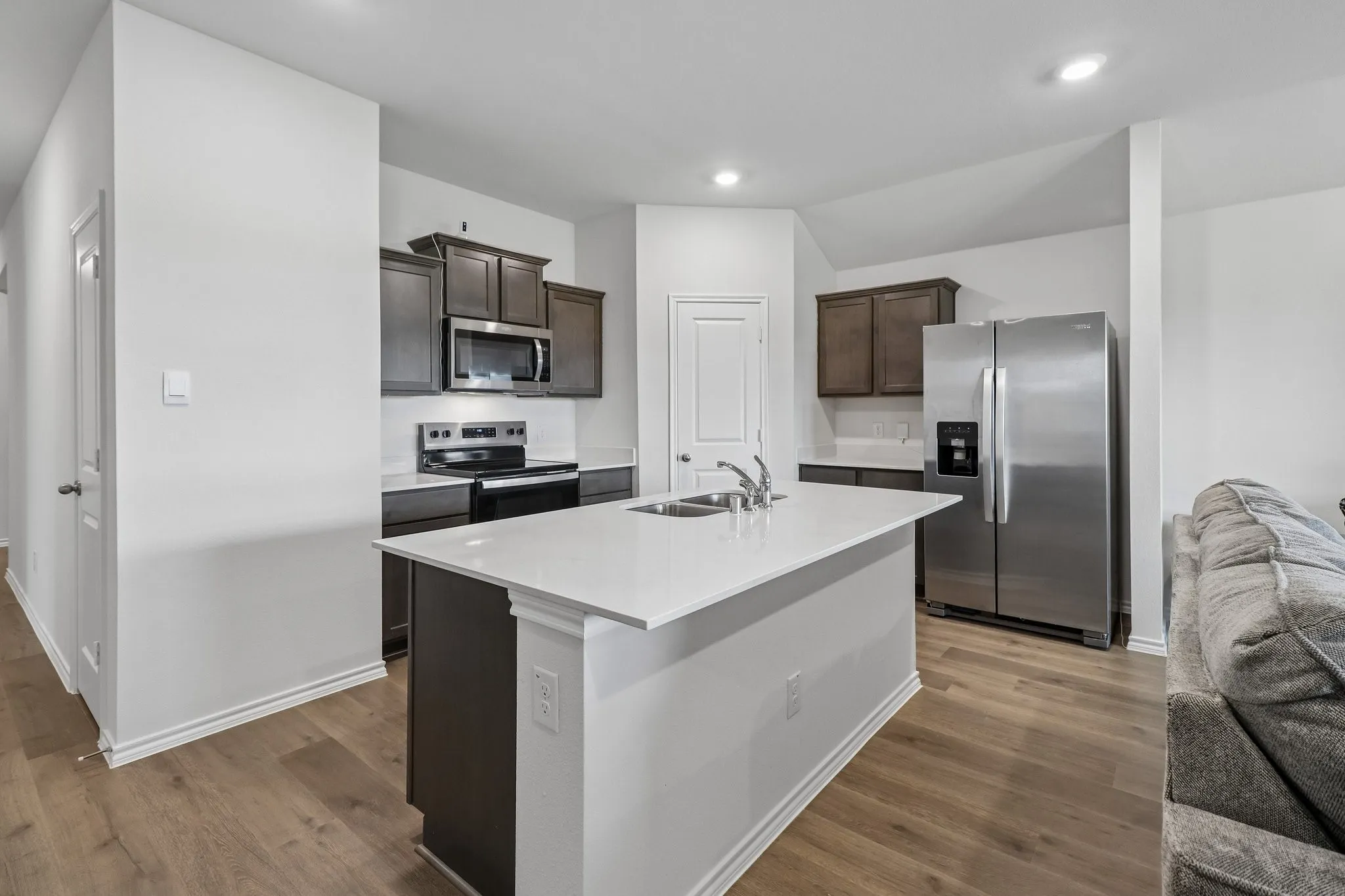 Kitchen featuring a central island with an integrated sink, white countertops, dark wood cabinetry, and stainless steel appliances including a refrigerator, range, and microwave